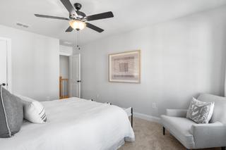 Spacious master bedroom in The Washington H townhome by Davidson Homes, white bedding, gray accent chair, ceiling fan, abstract wall art