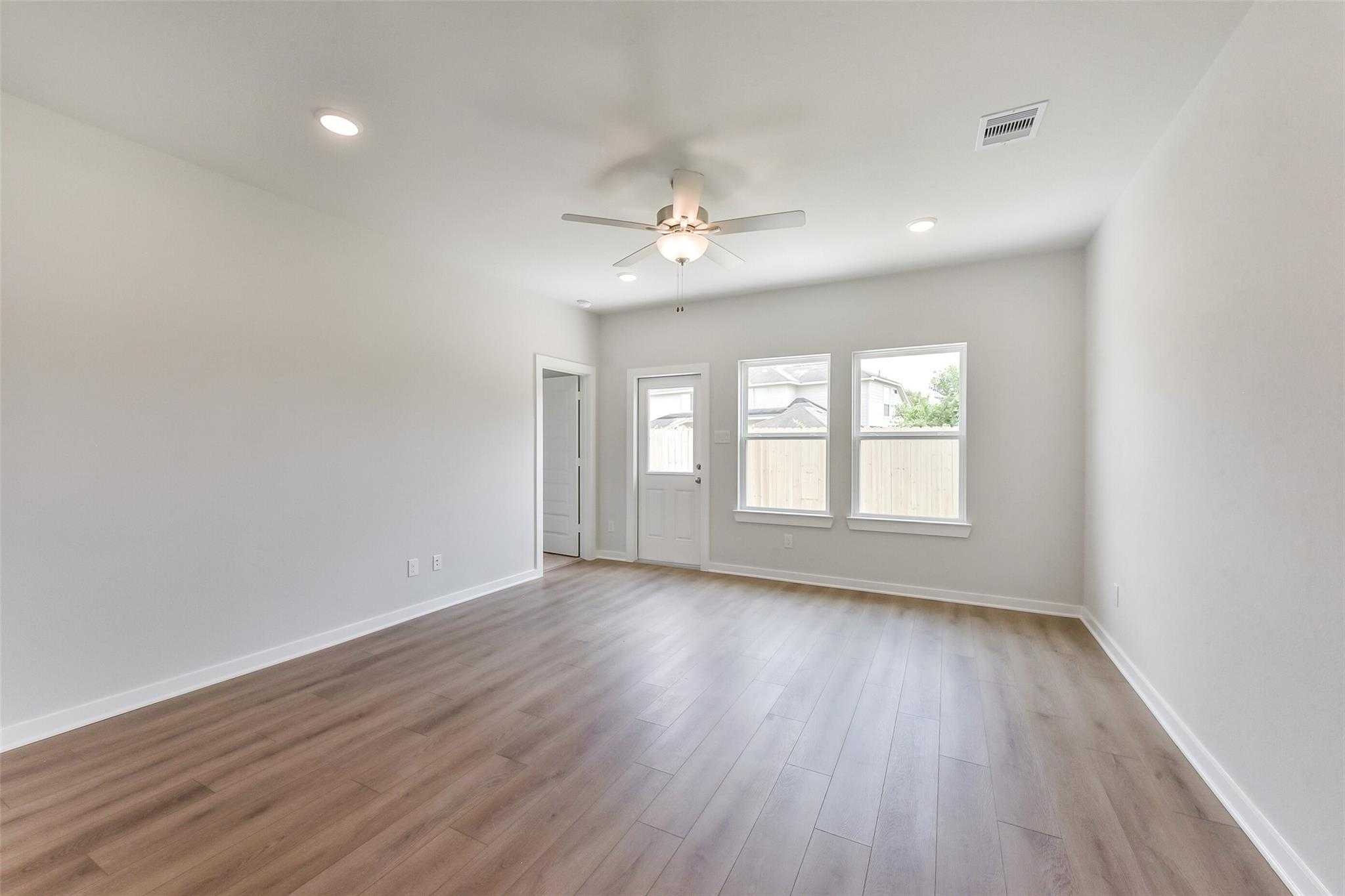 Spacious living room with ceiling fan, large windows, wood-look floors, and backyard door in Davidson Homes The Frio F, Dayton, TX