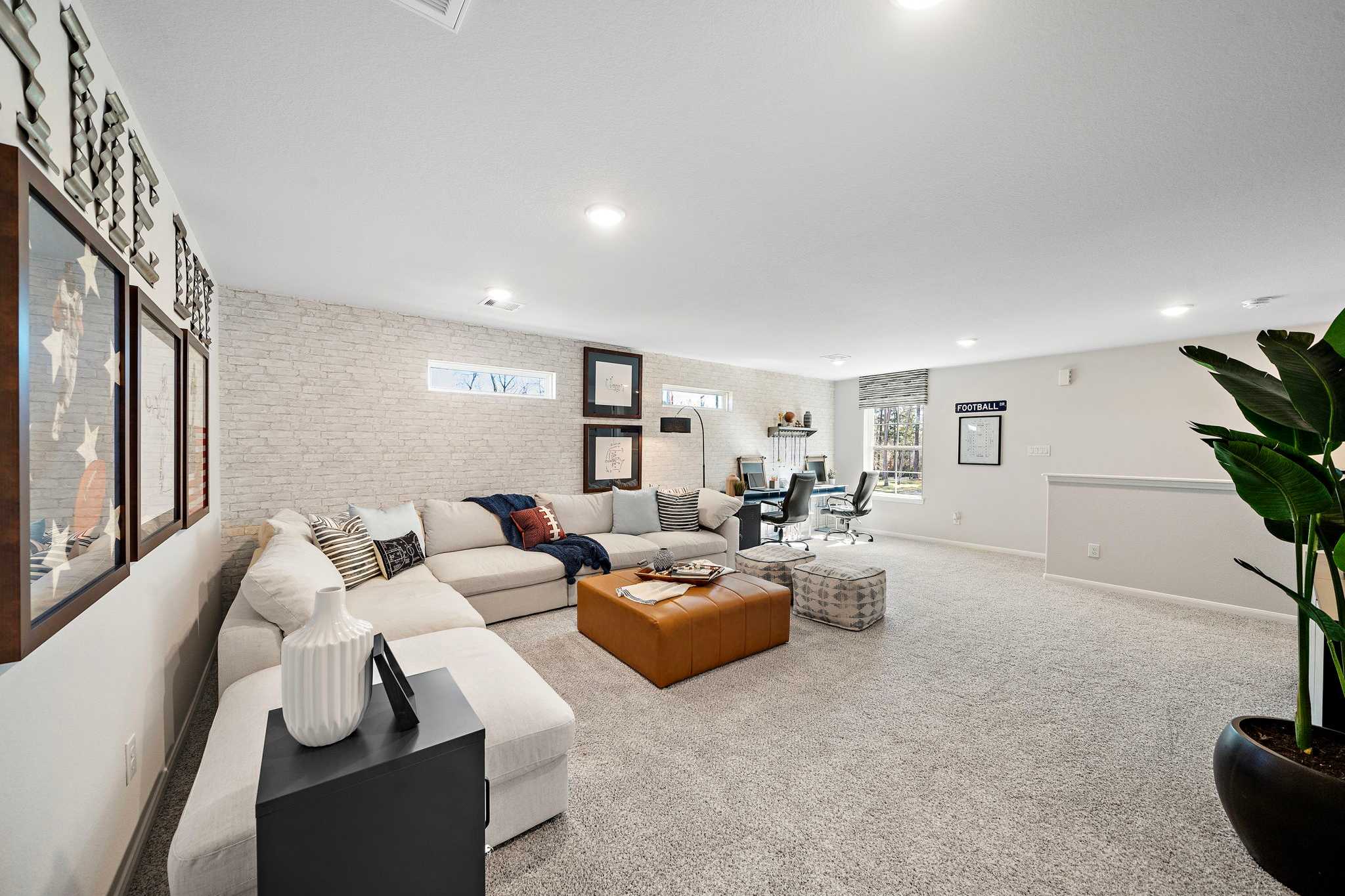 Spacious modern family room at Lakes at Black Oak in Magnolia Texas with L-shaped sofa, leather ottoman, desk nook, and potted plant