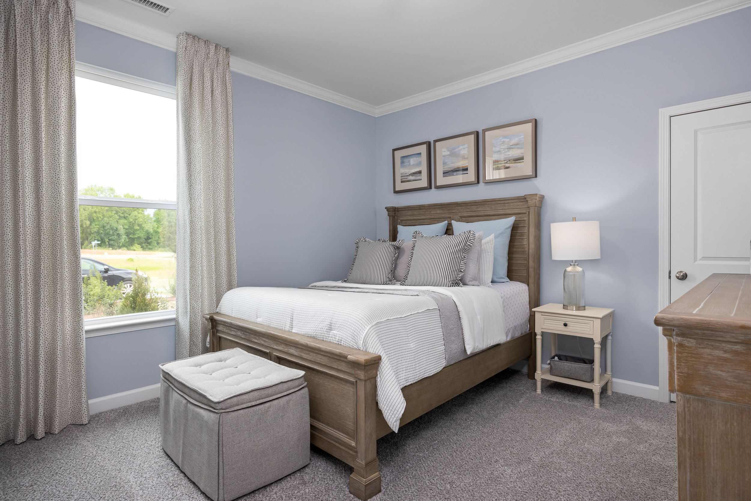 Cozy master bedroom in The Magnolia B featuring light blue walls, queen bed with blue pillows, wooden furniture, and large window