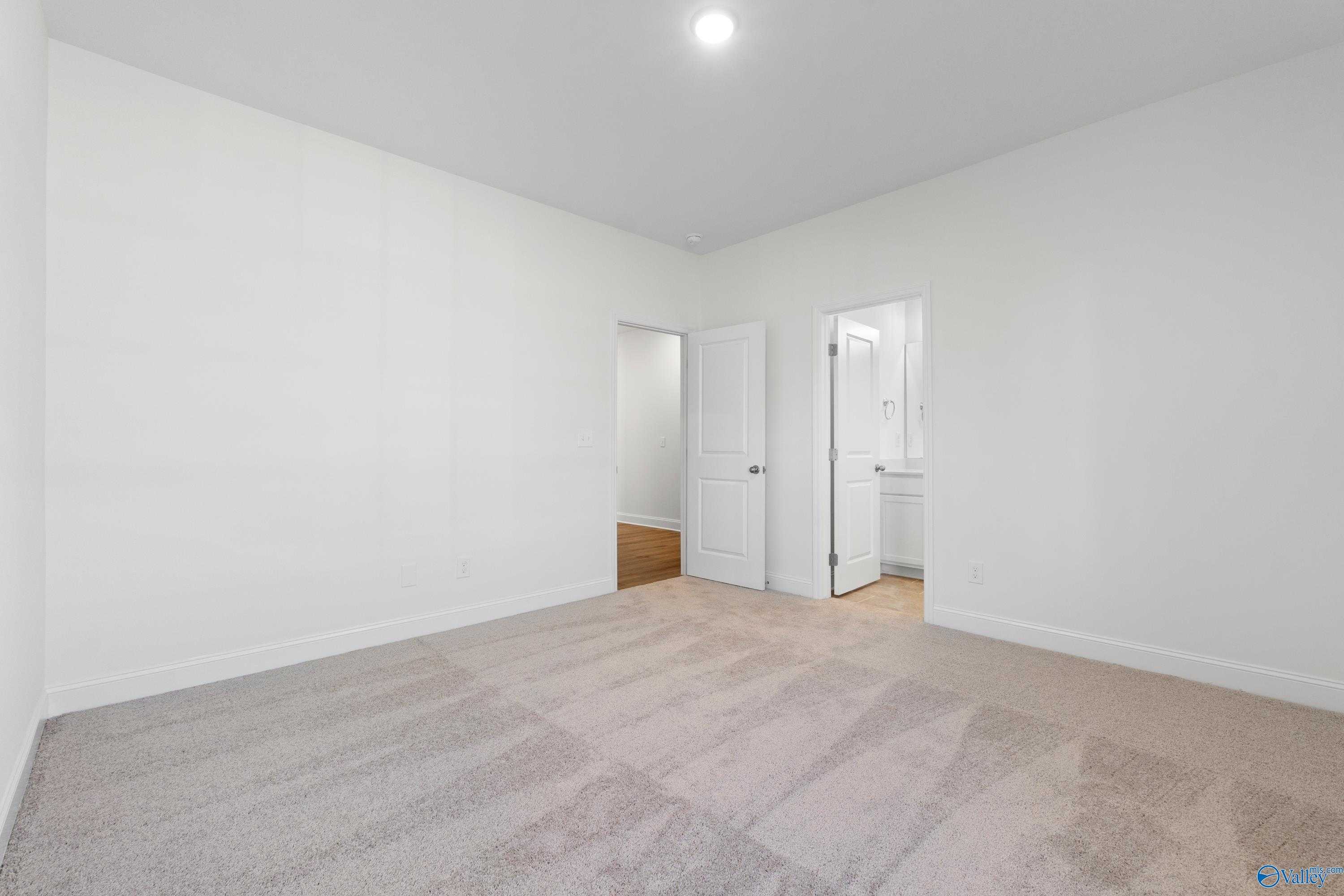 Bright secondary bedroom with beige carpet, white walls, and adjacent bathroom in Davidson Homes The Oxford, Creekside, Harvest, Alabama