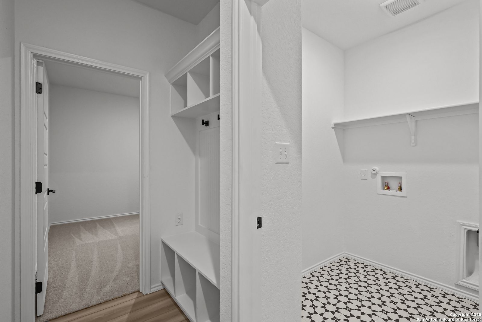 Bright laundry room with built-in cabinets, coat hooks, bench, washer/dryer space, and tiled floor in Davidson Homes The Daphne J, Converse, Texas