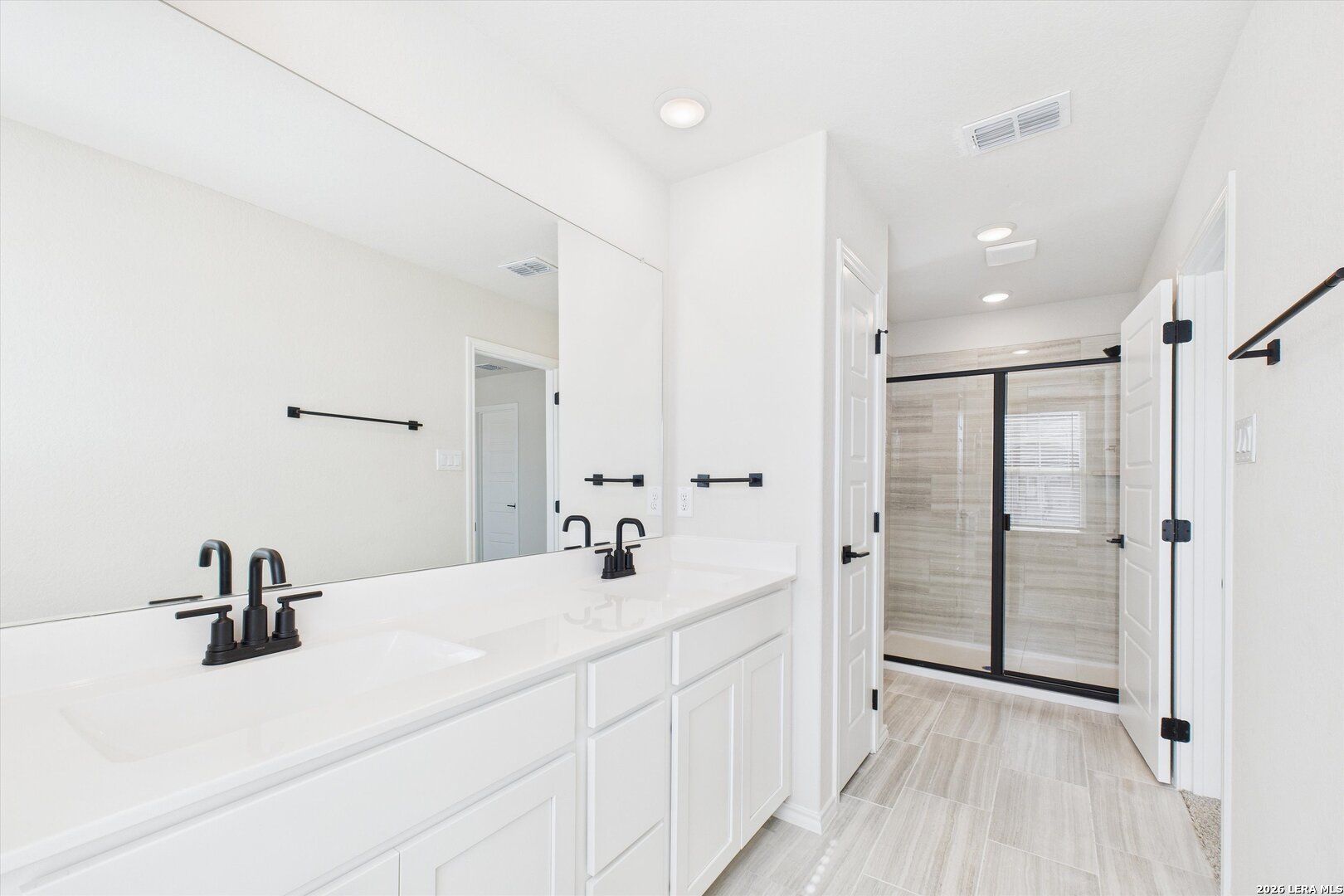 Modern master bath with double white vanity, black faucets, frameless mirror, and glass shower in Davidson Homes The Gillian B, San Antonio