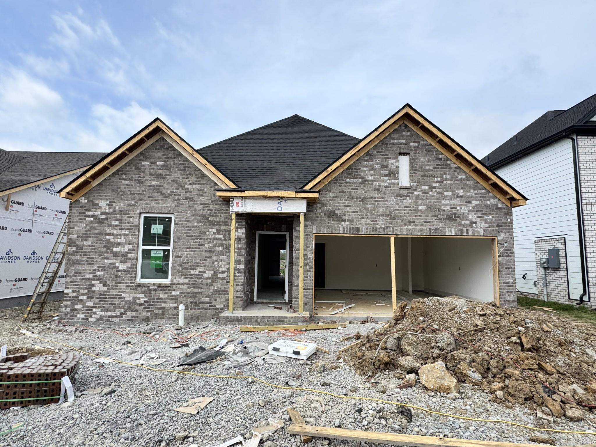 Single-story gray brick home under construction with 2-car garage and gabled roof, Davidson Homes Cottonwood E in Woods Crossing, Gallatin, TN