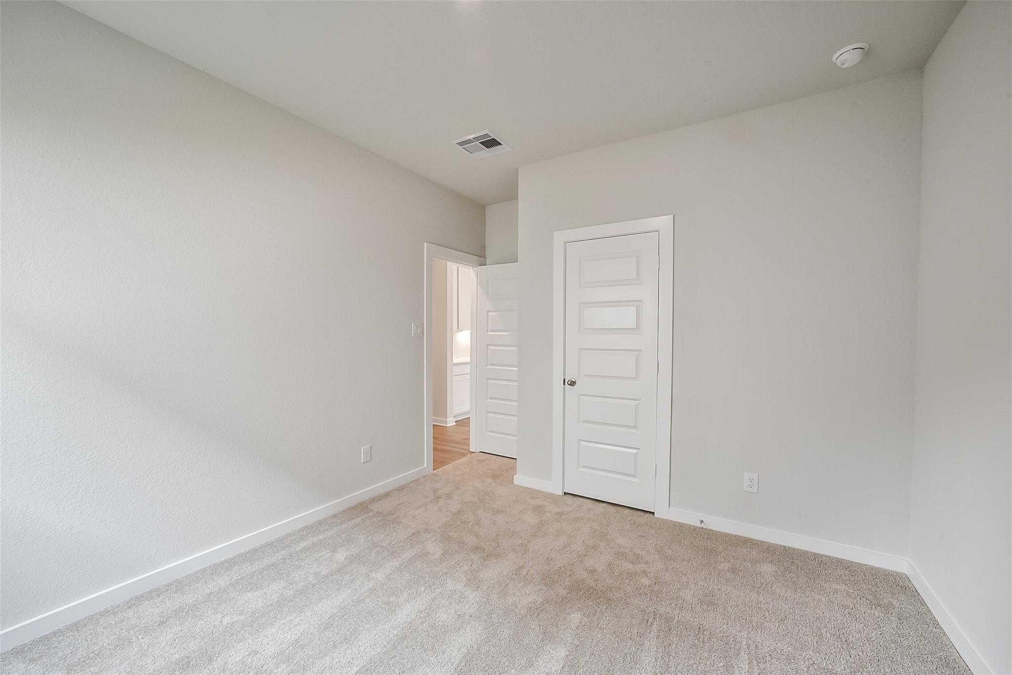 Spacious secondary bedroom with beige carpet, light gray walls, and en-suite bath access in Davidson Homes The Frio F, Conroe, TX