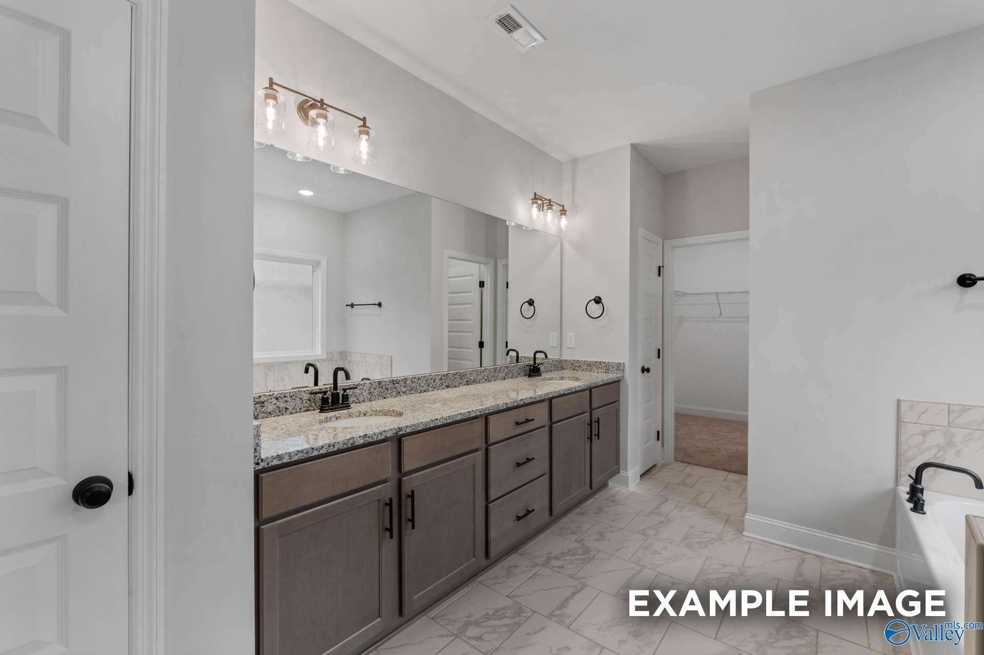 Elegant master bathroom with double granite vanity, mirrored sconces, and tile floor in Davidson Homes The Finleigh, Meridianville