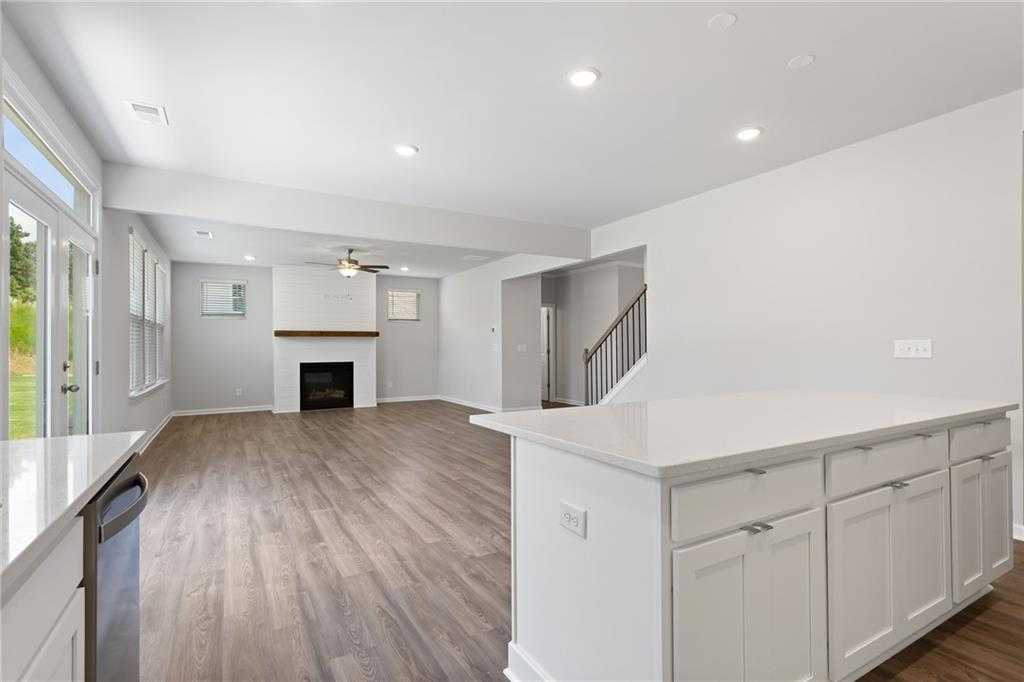 Open-concept great room with white stone fireplace, kitchen island, hardwood floors in Davidson Homes The Hickory B, Winder, GA