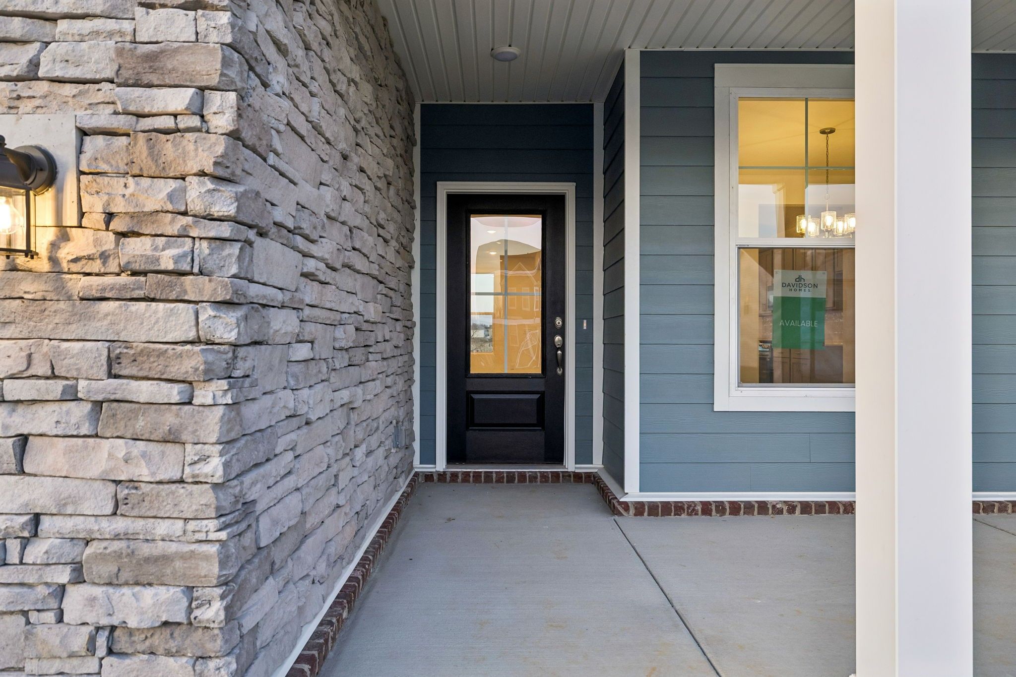 Covered front porch with stone accent wall and black glass door at Davidson Homes' The Willow A in Calista Farms, White House, TN