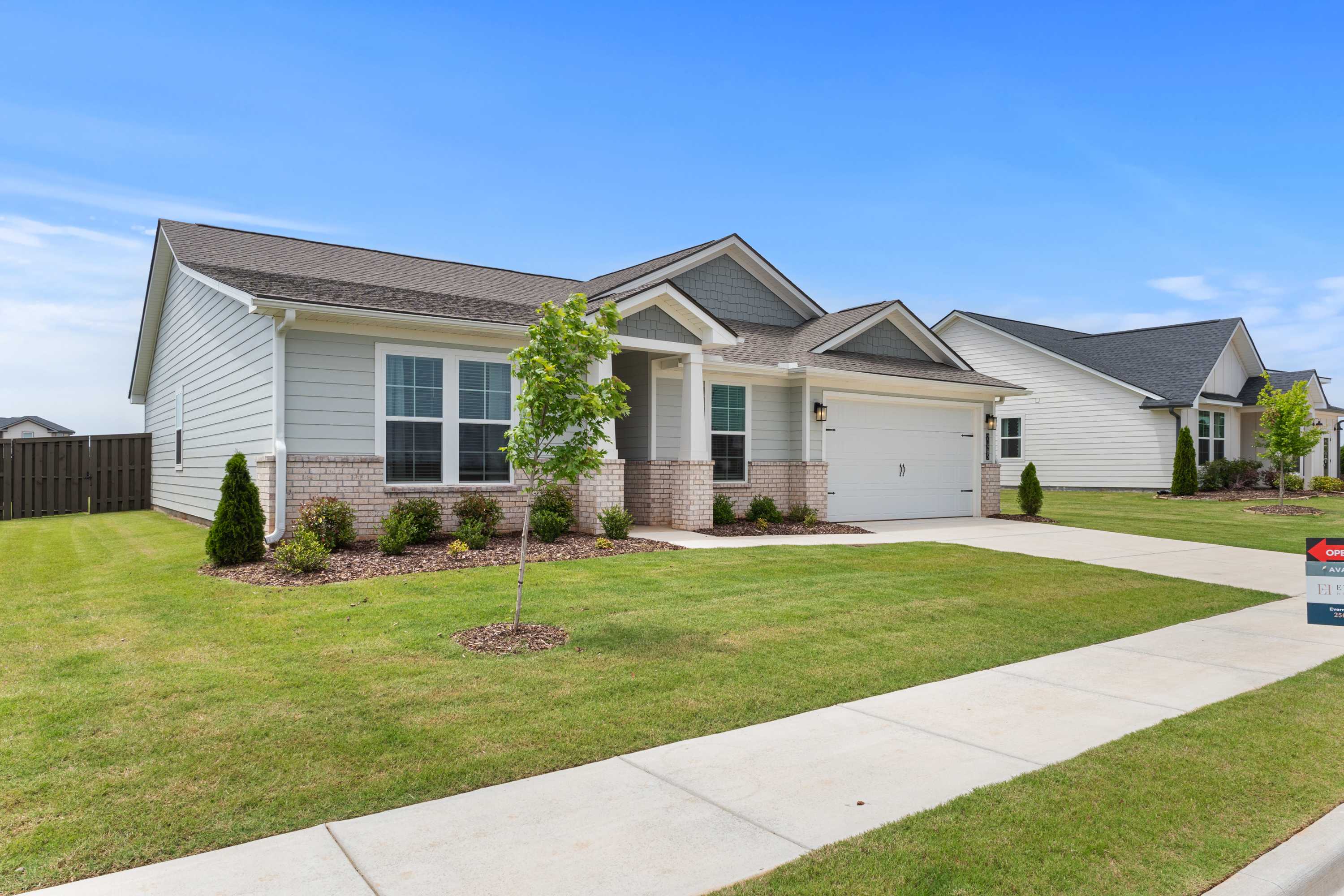 Contemporary ranch-style home exterior at Anderson Farm in Athens AL by Davidson Homes with white siding, brick base, and landscaped yard