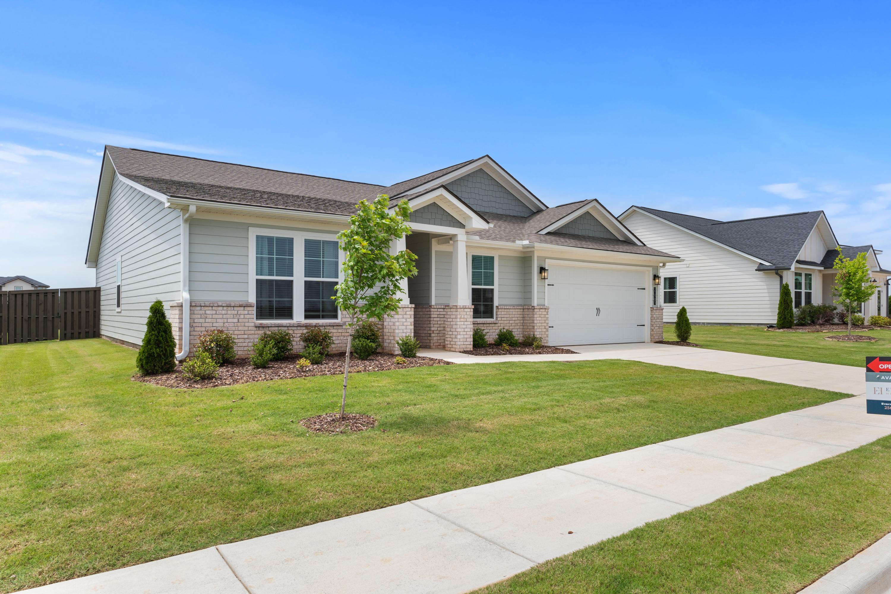 Contemporary ranch-style home exterior at Anderson Farm in Athens AL by Davidson Homes with white siding, brick base, and landscaped yard