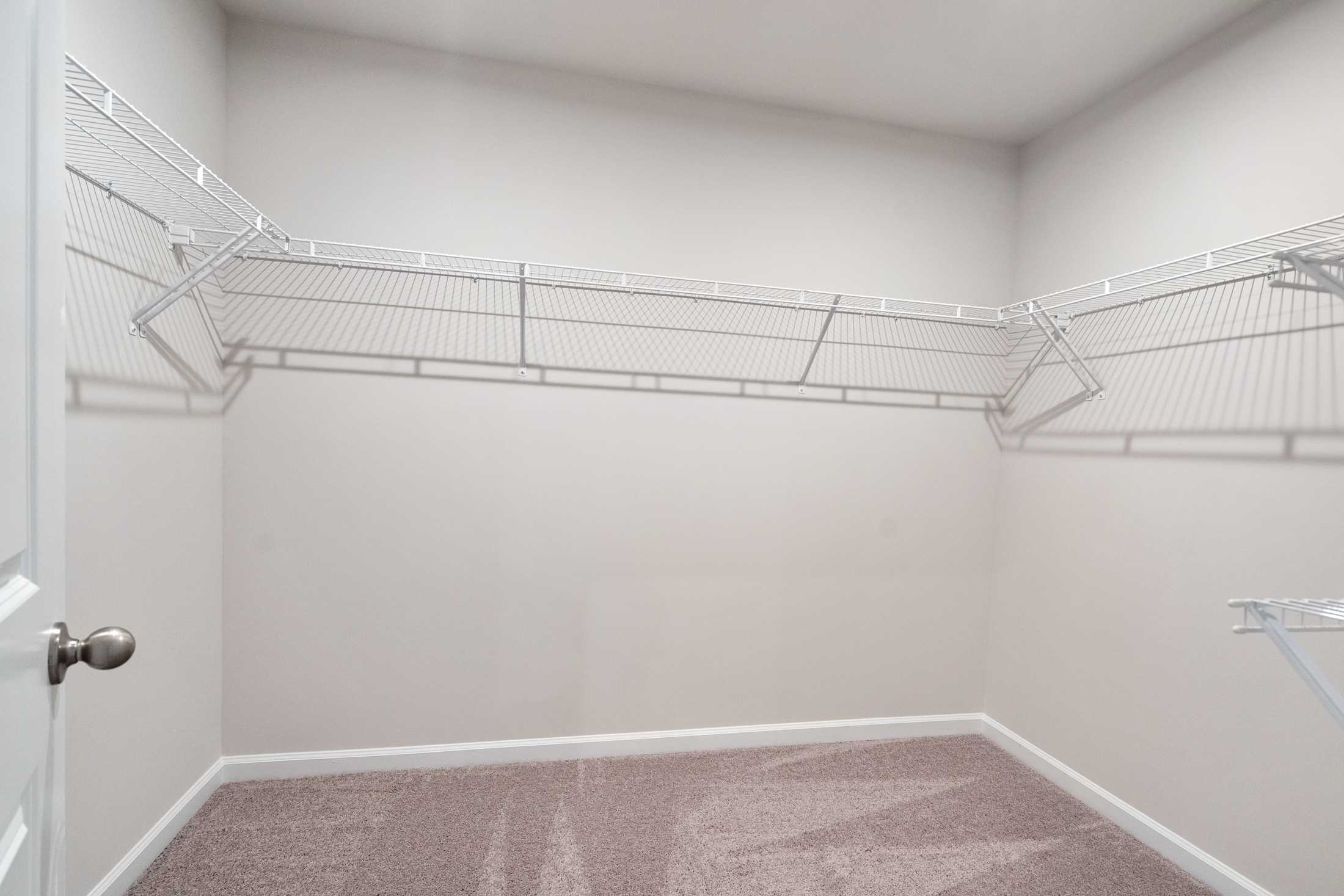 Spacious walk-in closet in The Cary B master suite featuring wire shelving, beige walls, and carpeted floor