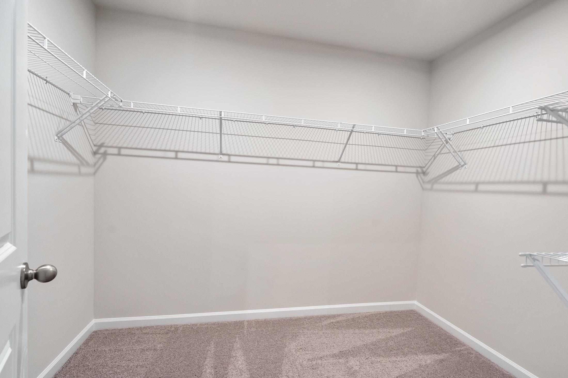 Spacious walk-in closet in The Cary B master suite featuring wire shelving, beige walls, and carpeted floor