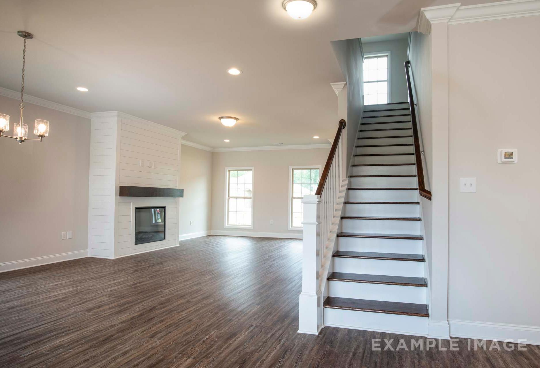 Open-concept living room in The Charleston 2-story home featuring modern fireplace, hardwood floors, and curved staircase