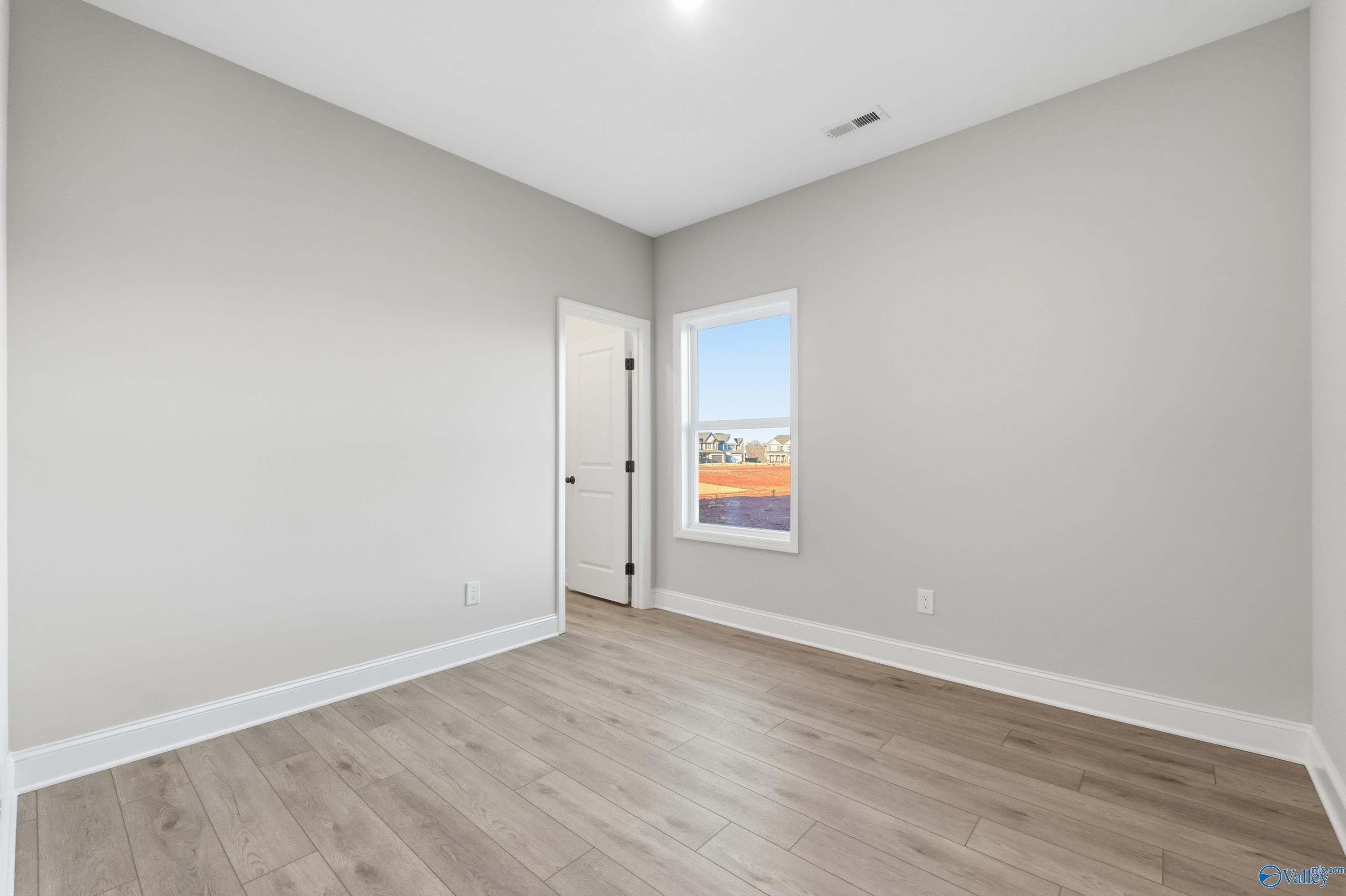 Bright secondary bedroom featuring gray walls, wood laminate flooring, and large window in Davidson Homes The Daphne C, Athens, Alabama