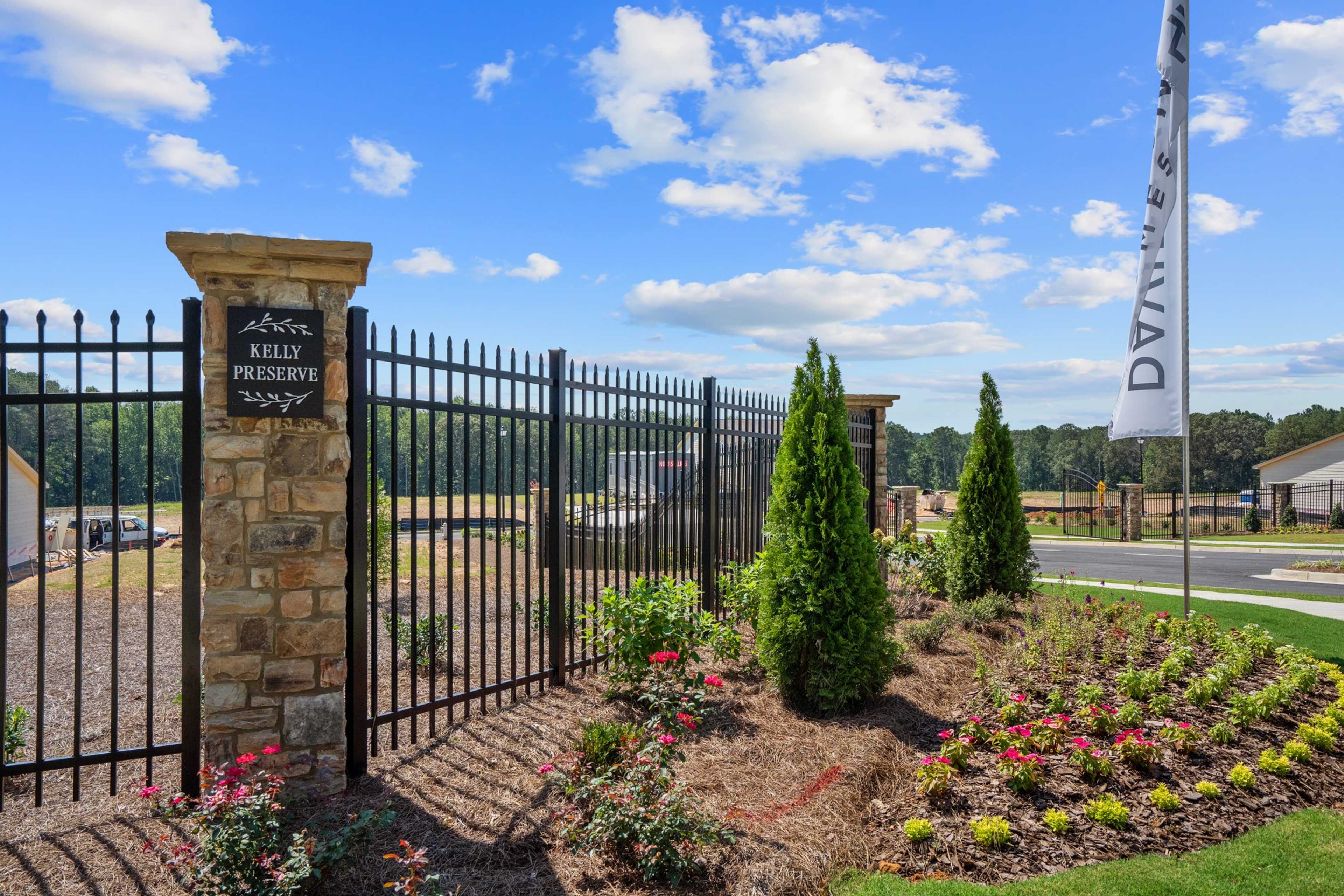 Gated entrance at Kelly Preserve in Loganville GA featuring stone pillars, wrought iron fence, Davidson Homes flags, and landscaped shrubs
