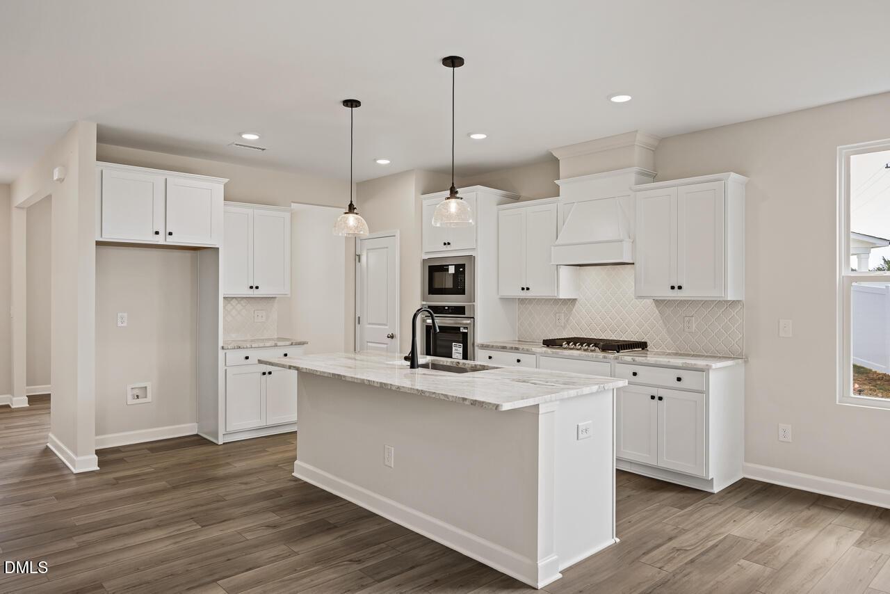 Modern kitchen with white cabinets, stone island, and stainless appliances in The Ash C floor plan at Woodland Crossing.