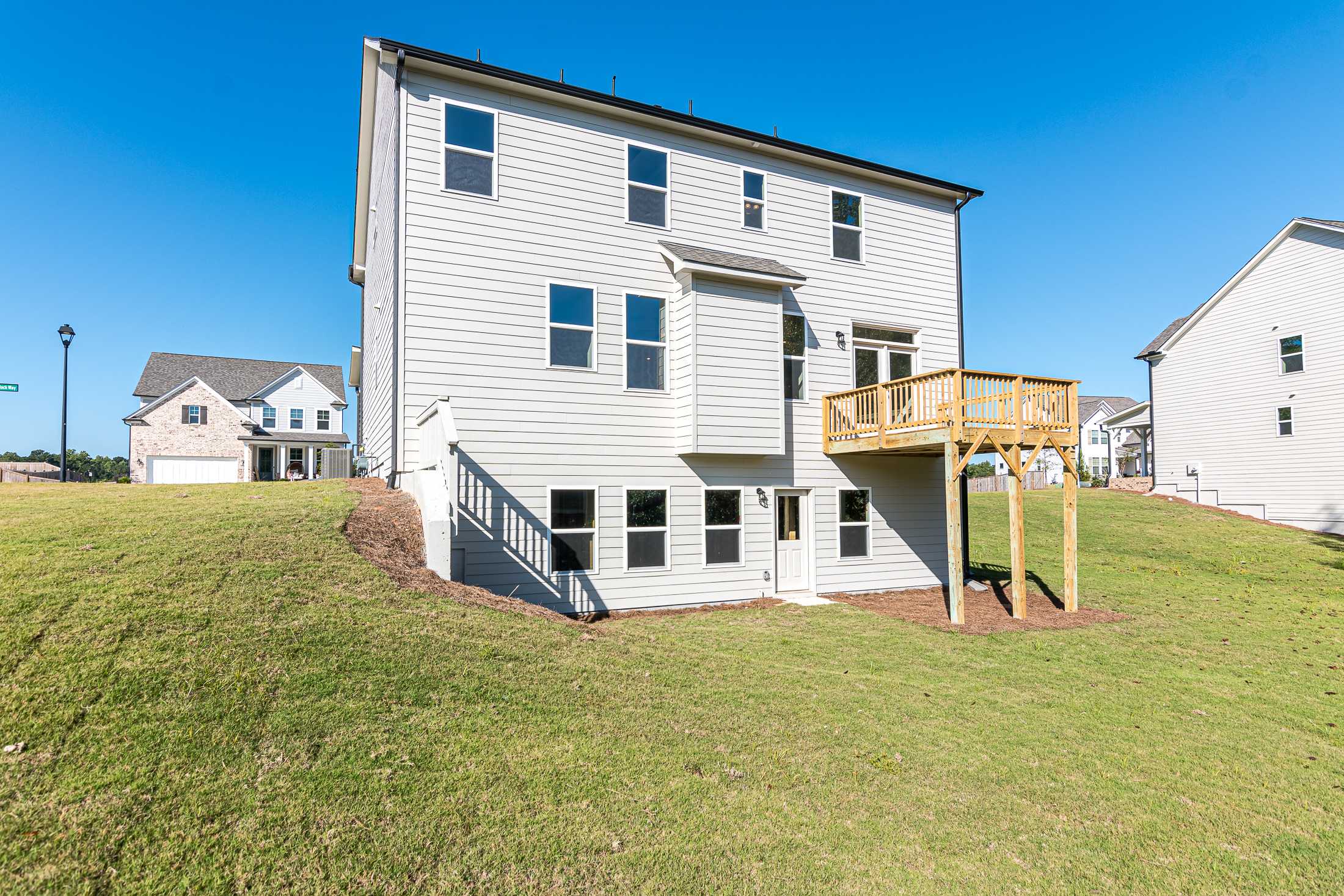 Rear elevation of The Willow B two-story home with upper deck, white siding, and lush backyard at Wehunt Meadows in Hoschton, Georgia