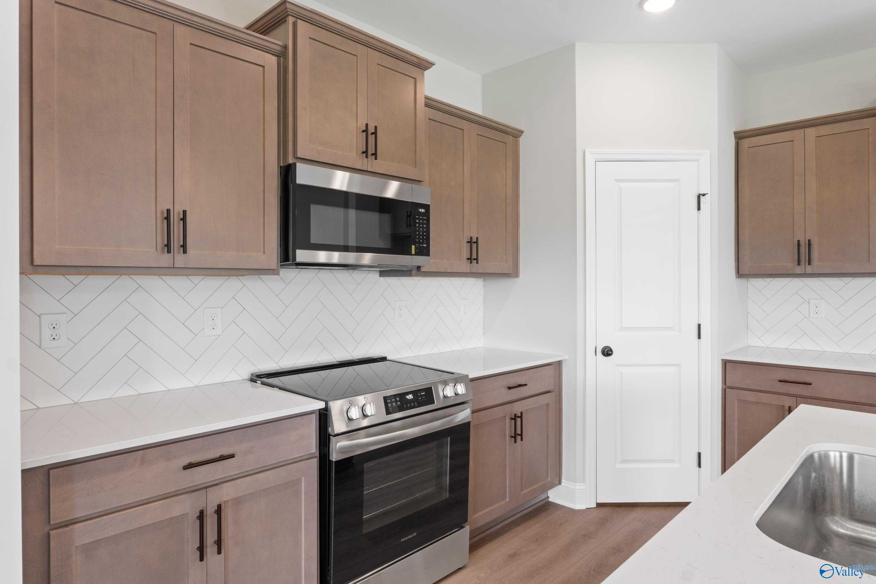 Modern kitchen with warm shaker cabinets, herringbone tile backsplash, stainless steel appliances in Davidson Homes The Franklin C, Hazel Green, AL