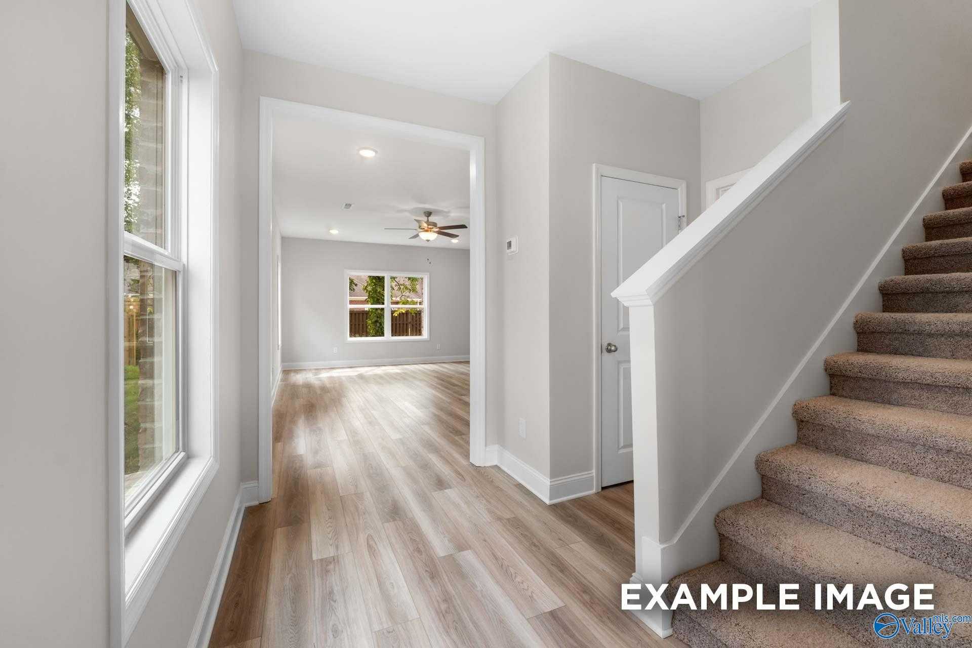 Bright entry hallway with light hardwood floors, arched doorway, ceiling fan, and carpeted staircase in The Camden home, Huntsville, Alabama