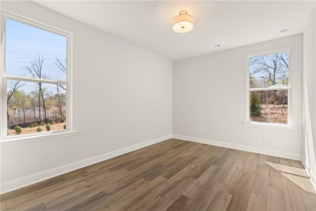 Bright empty bedroom with light hardwood floors, white walls, and large windows overlooking wooded yard in Davidson Homes The Danbury C, Buford, GA