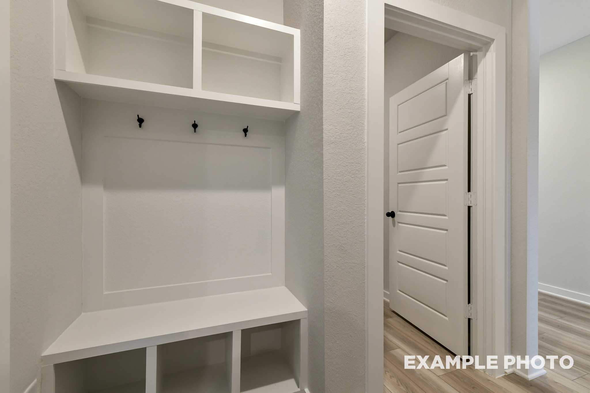 Modern mudroom in The Daphne G featuring white built-in cabinetry, open shelves, coat hooks, bench, and adjacent doorway