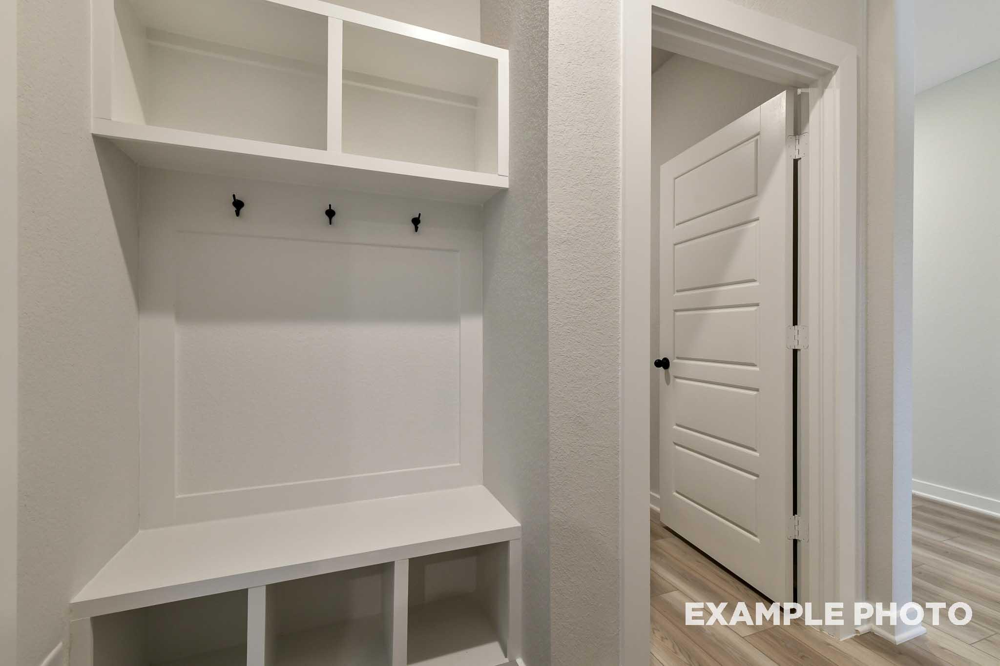 Modern mudroom in The Daphne G featuring white built-in cabinetry, open shelves, coat hooks, bench, and adjacent doorway