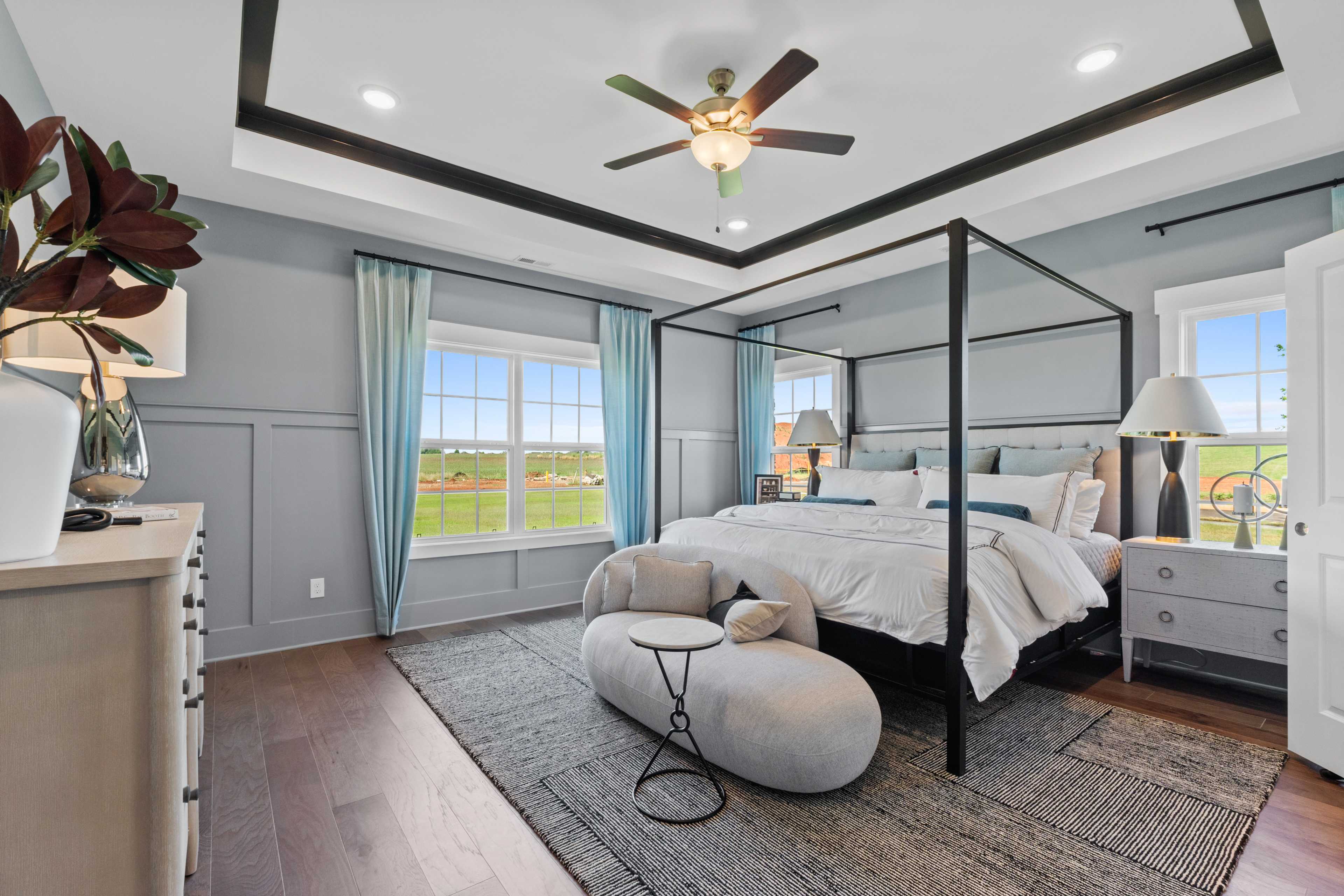 Spacious primary bedroom at Creekside in Harvest Alabama with canopy bed, hardwood floors, and scenic field views