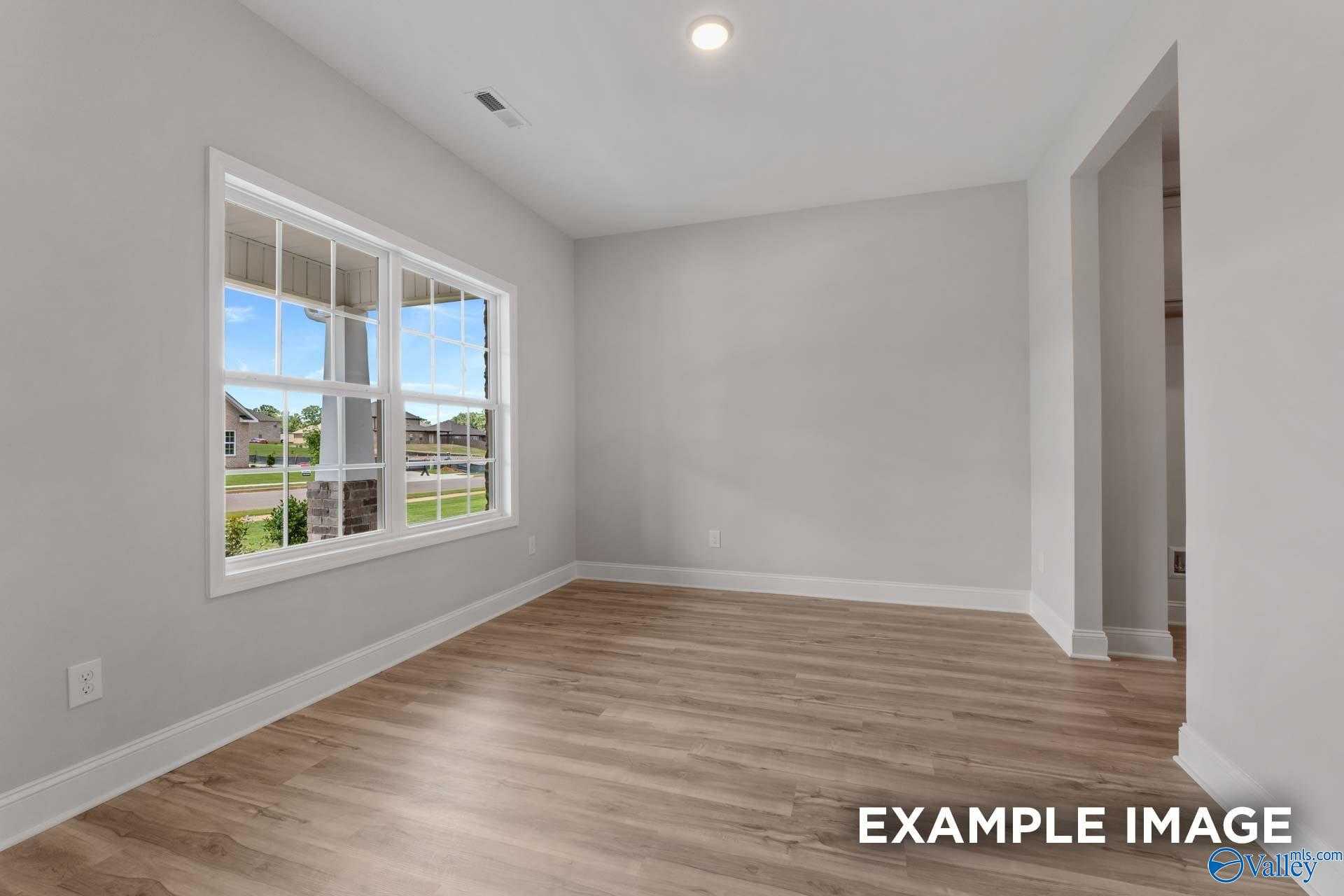 Bright empty living room with large windows, light gray walls, hardwood floors in Davidson Homes The Shelby C, Meridianville AL