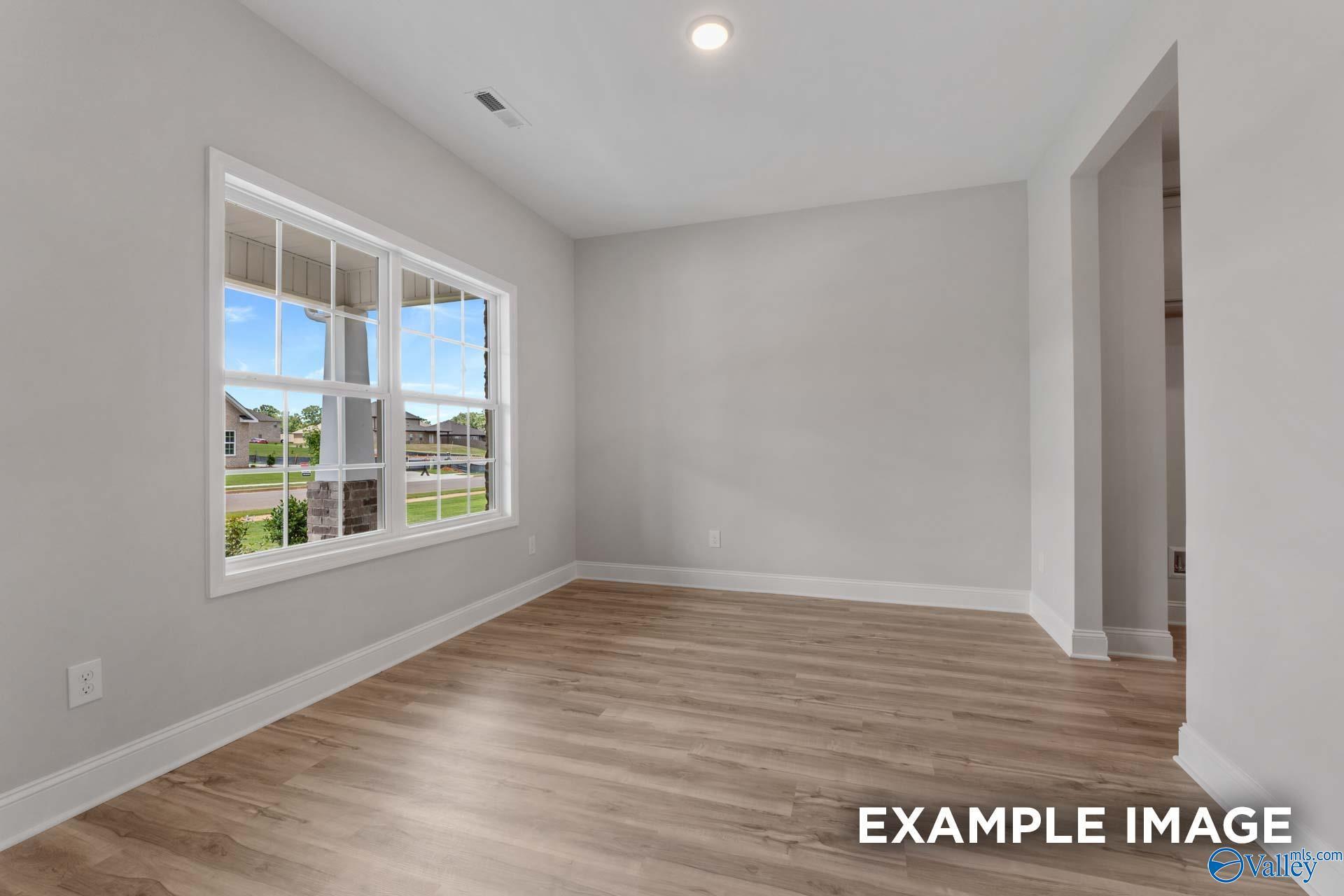 Bright empty living room with large windows, light gray walls, hardwood floors in Davidson Homes The Shelby C, Meridianville AL