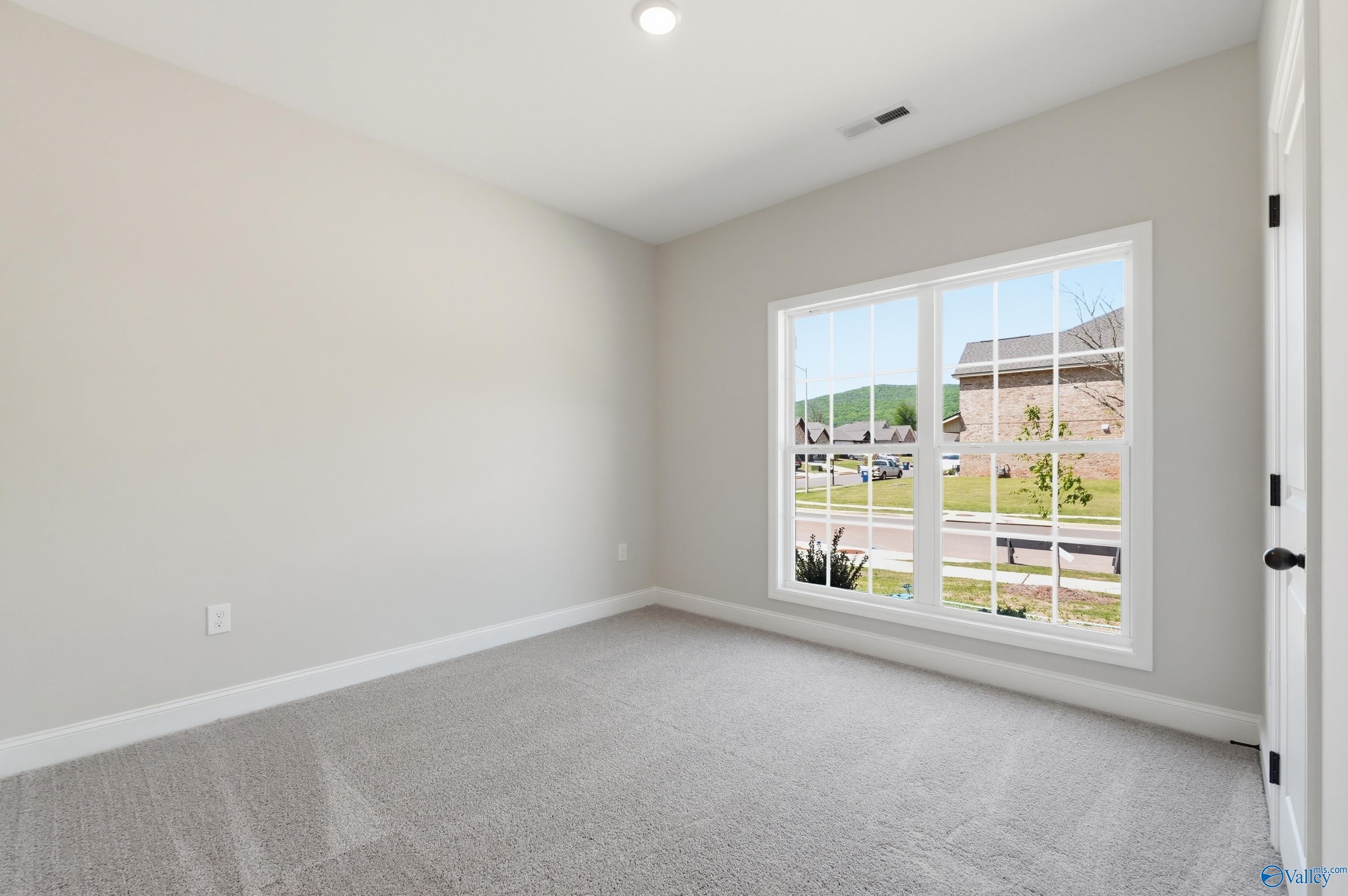 Bright secondary bedroom with large window view of neighborhood hills, neutral walls, gray carpet in The Franklin home, Huntsville