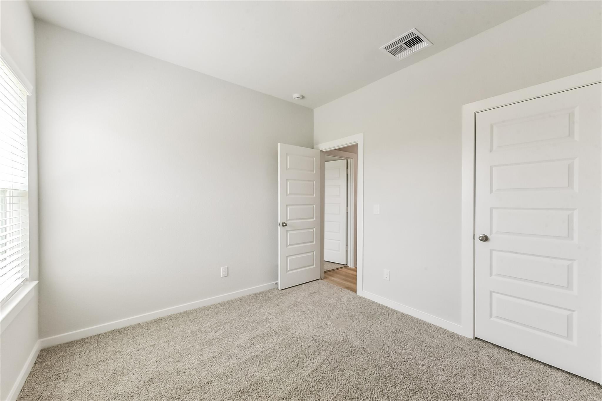 Bright secondary bedroom with neutral gray walls, beige carpet, open door to hallway in Davidson Homes The Frio G, Magnolia TX