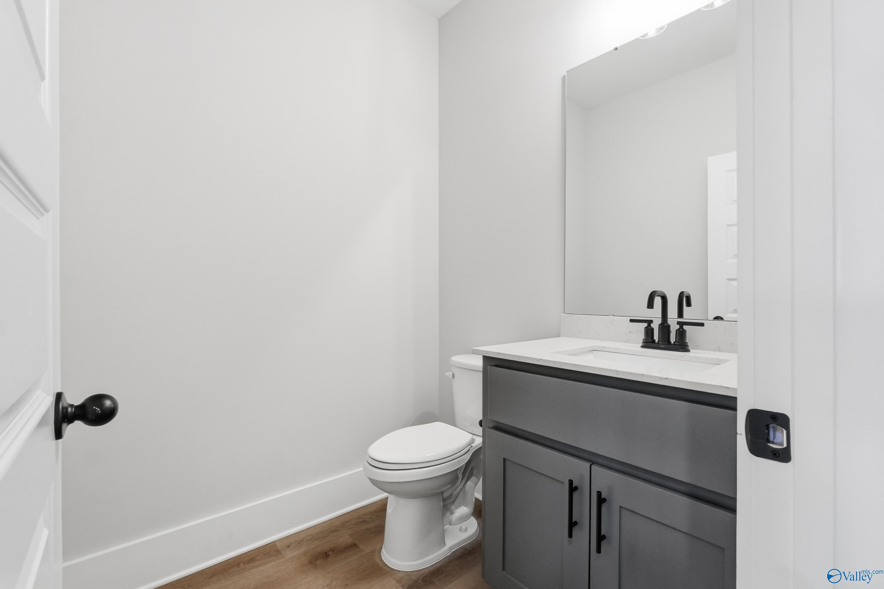 Elegant powder room with gray vanity, white sink, toilet, and large mirror in Davidson Homes The Finleigh, Meridianville, Alabama