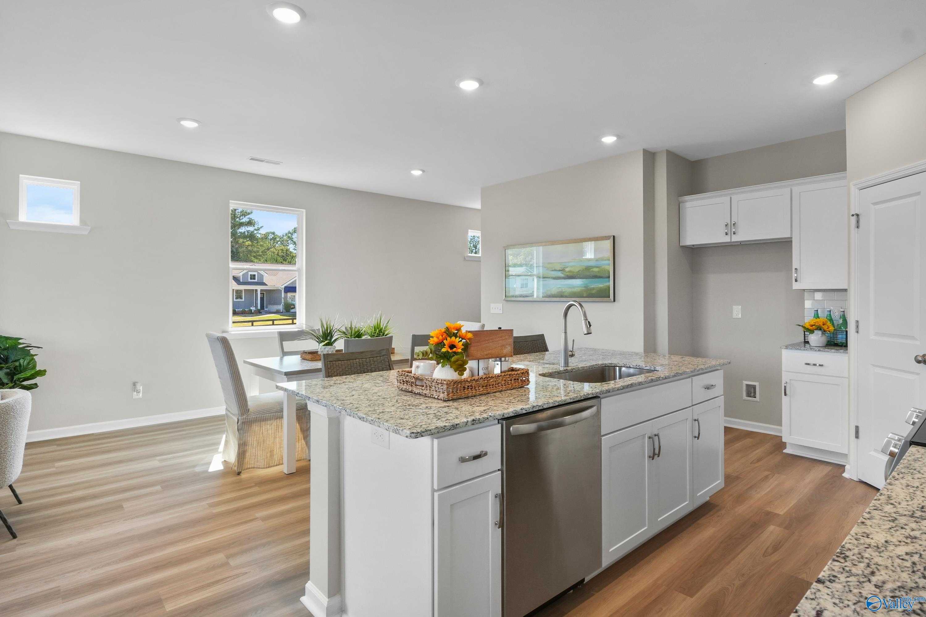 Open-concept kitchen with white cabinets, granite island sink, stainless dishwasher, and dining table in Evermore Homes The Malibu, Madison Alabama