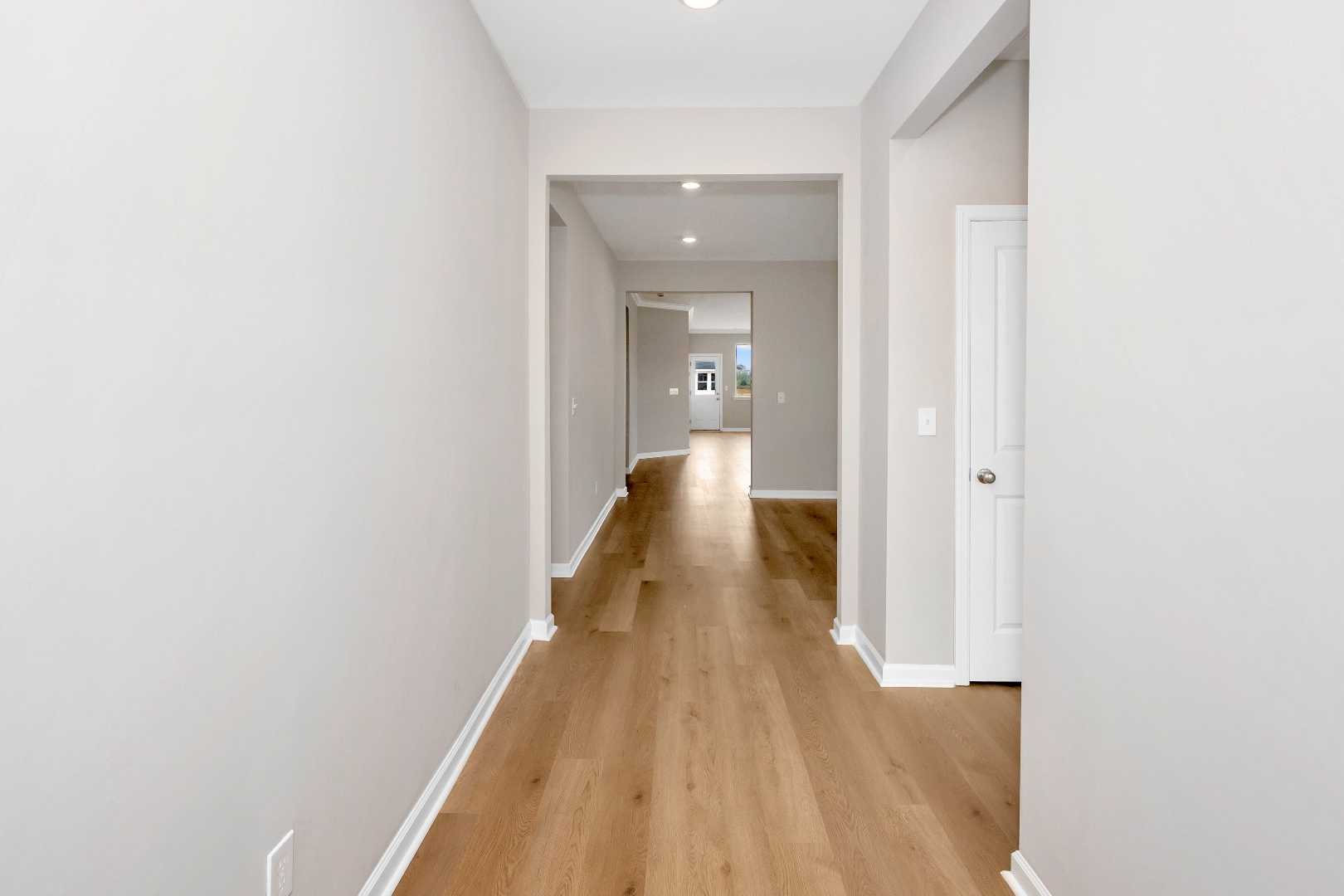Spacious main floor hallway in The Orion home by Evermore Homes, light gray walls, oak hardwood floors