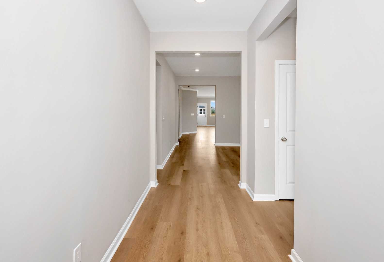 Spacious main floor hallway in The Orion home by Evermore Homes, light gray walls, oak hardwood floors