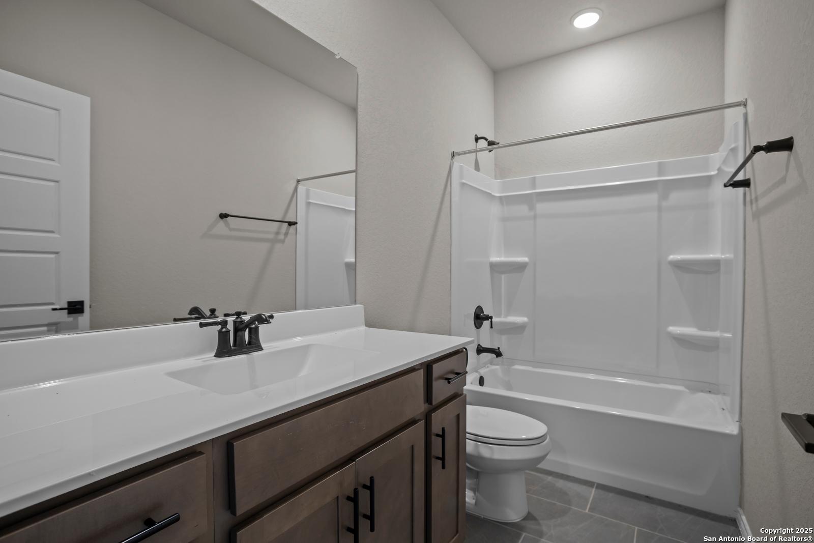 Modern bathroom with white tiled tub-shower combo, wooden vanity, and mirror in Davidson Homes The Asheville H, Converse, Texas