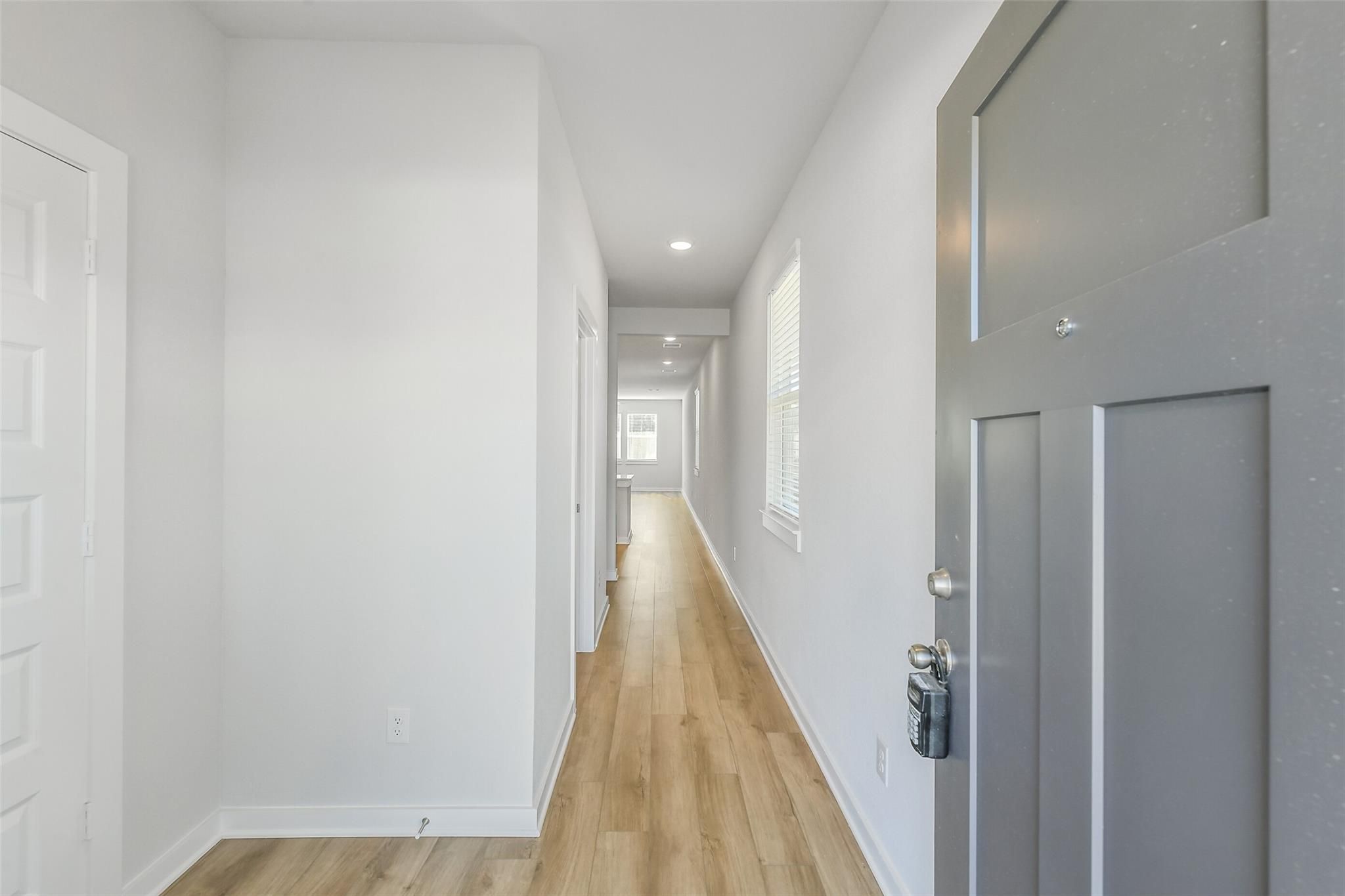 Bright entry hallway with light oak floors, white walls, side doors, and gray front door in Davidson Homes The San Marcos E, Cleveland, Texas