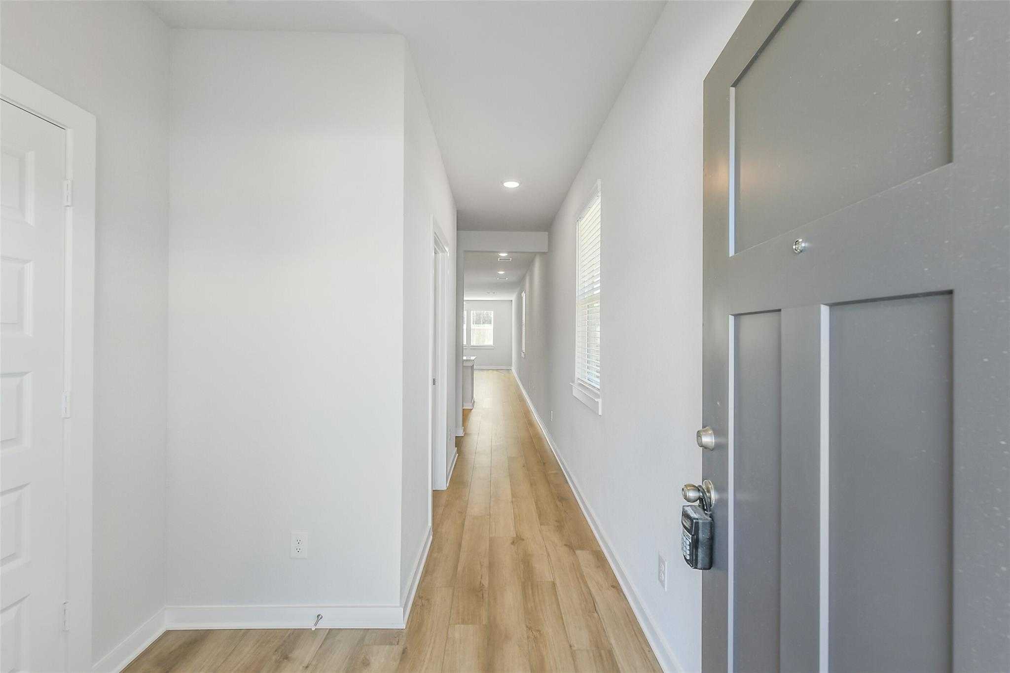 Bright entry hallway with light oak floors, white walls, side doors, and gray front door in Davidson Homes The San Marcos E, Cleveland, Texas