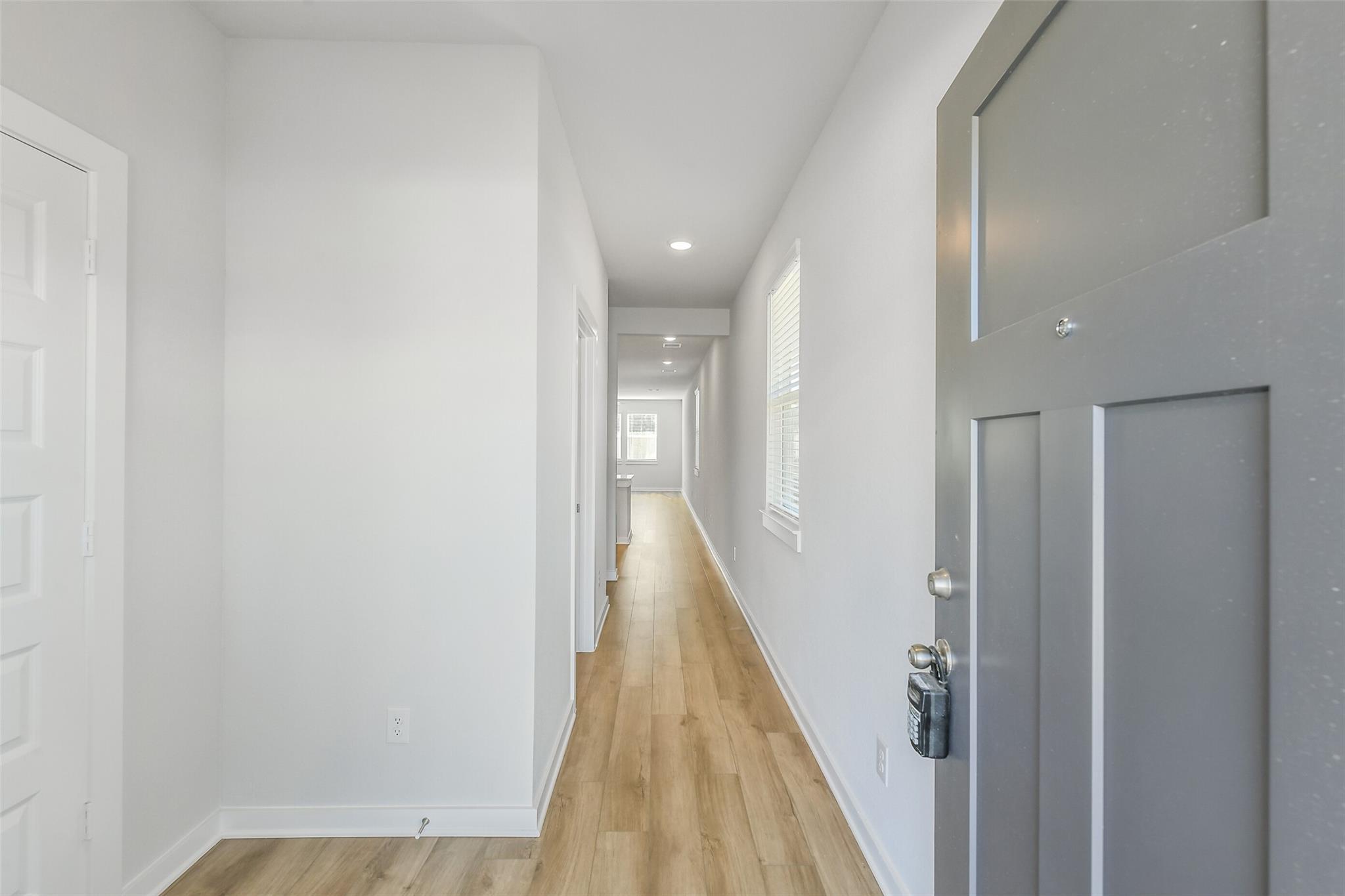 Bright entry hallway with light oak floors, white walls, side doors, and gray front door in Davidson Homes The San Marcos E, Cleveland, Texas