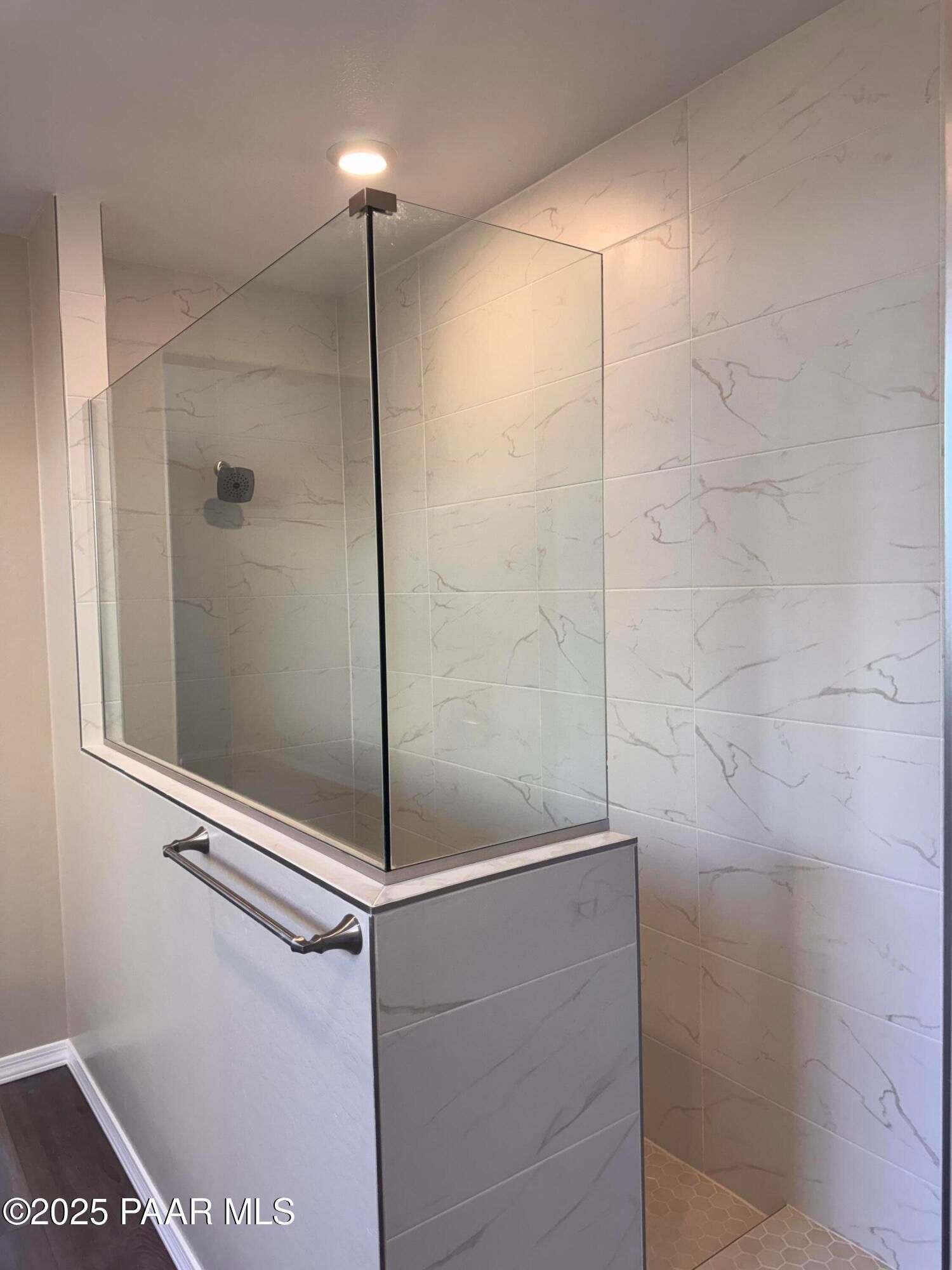 Modern frameless glass shower enclosure with white marble tiles, rainfall showerhead, and grab bar in Davidson Homes The Sunrise II A, Prescott, Arizona