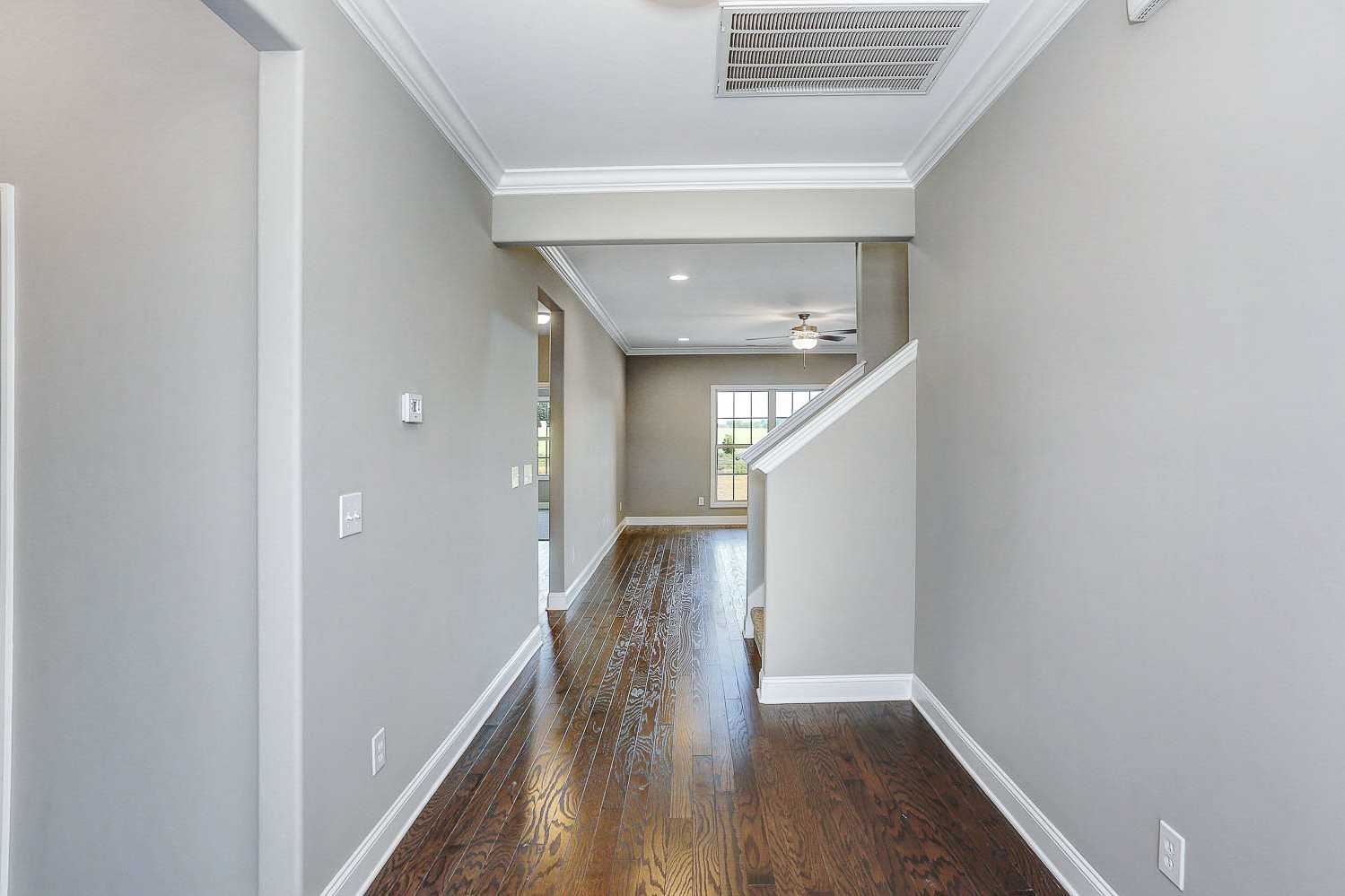 Spacious hallway in The Montgomery home by Davidson Homes with oak hardwood floors, gray walls, and open staircase to main living area