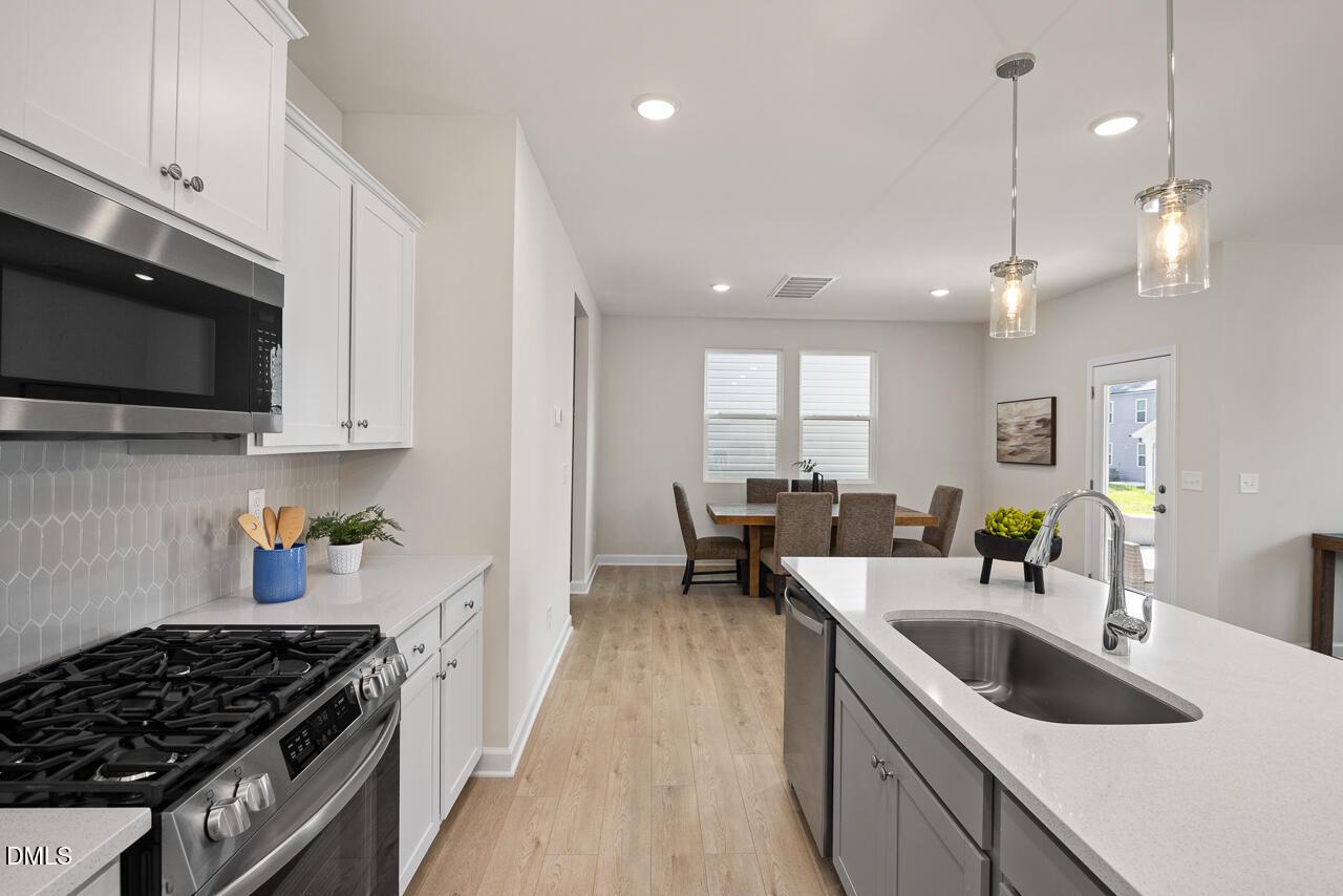 Modern open-concept kitchen with white cabinets, stainless appliances, herringbone backsplash, and adjacent dining area in The Preston A, Lillington, NC