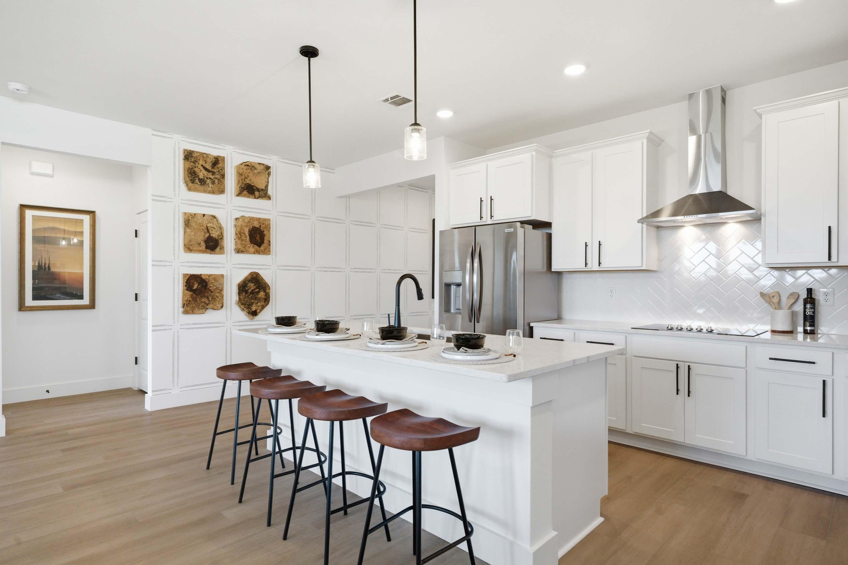 Modern white kitchen in The Laurel featuring a spacious island, pendant lighting, and stylish wood bar stools.