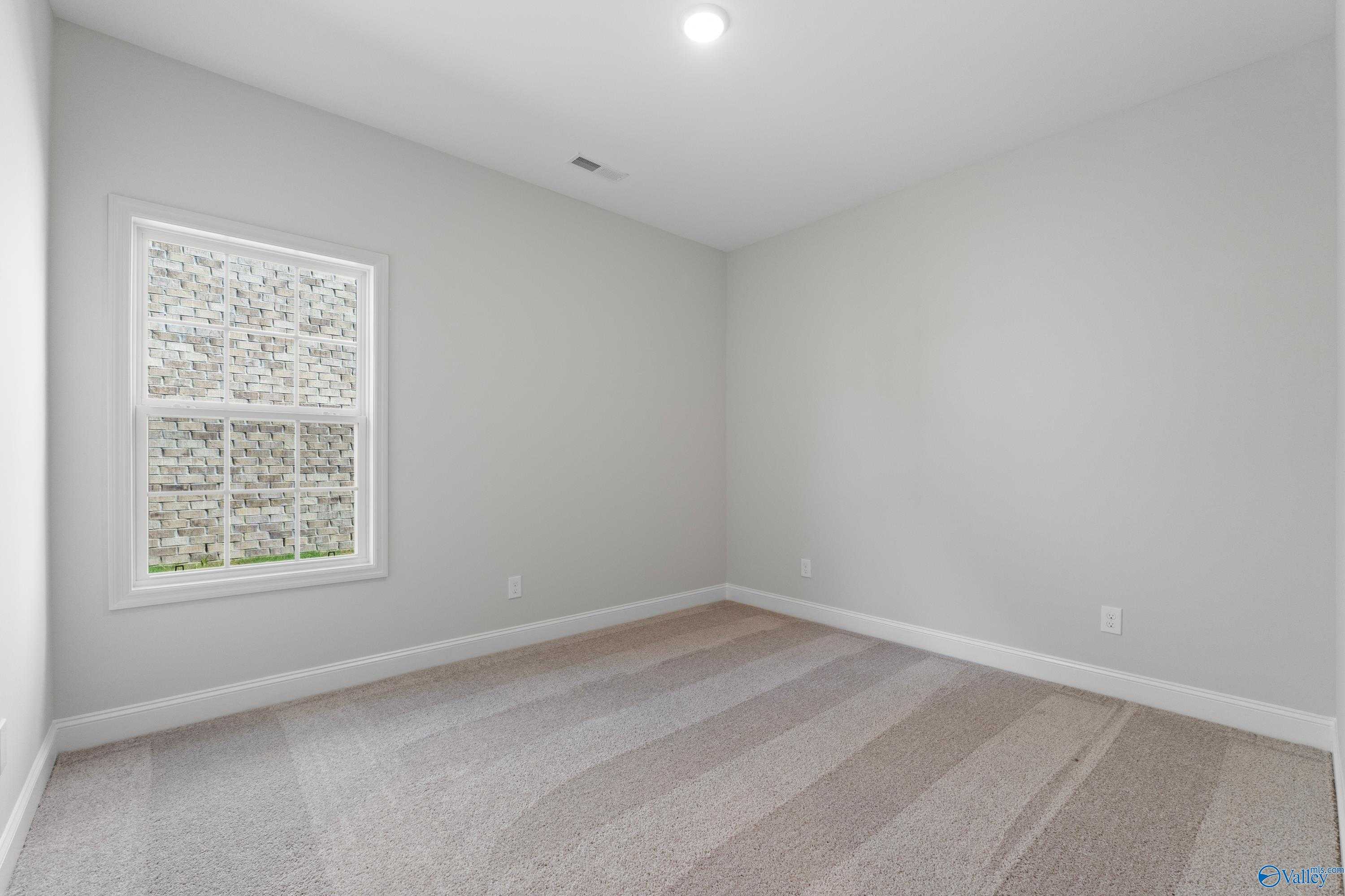 Bright bedroom with large window, neutral gray walls, and plush carpet in Davidson Homes The Rockford, Toney, Alabama