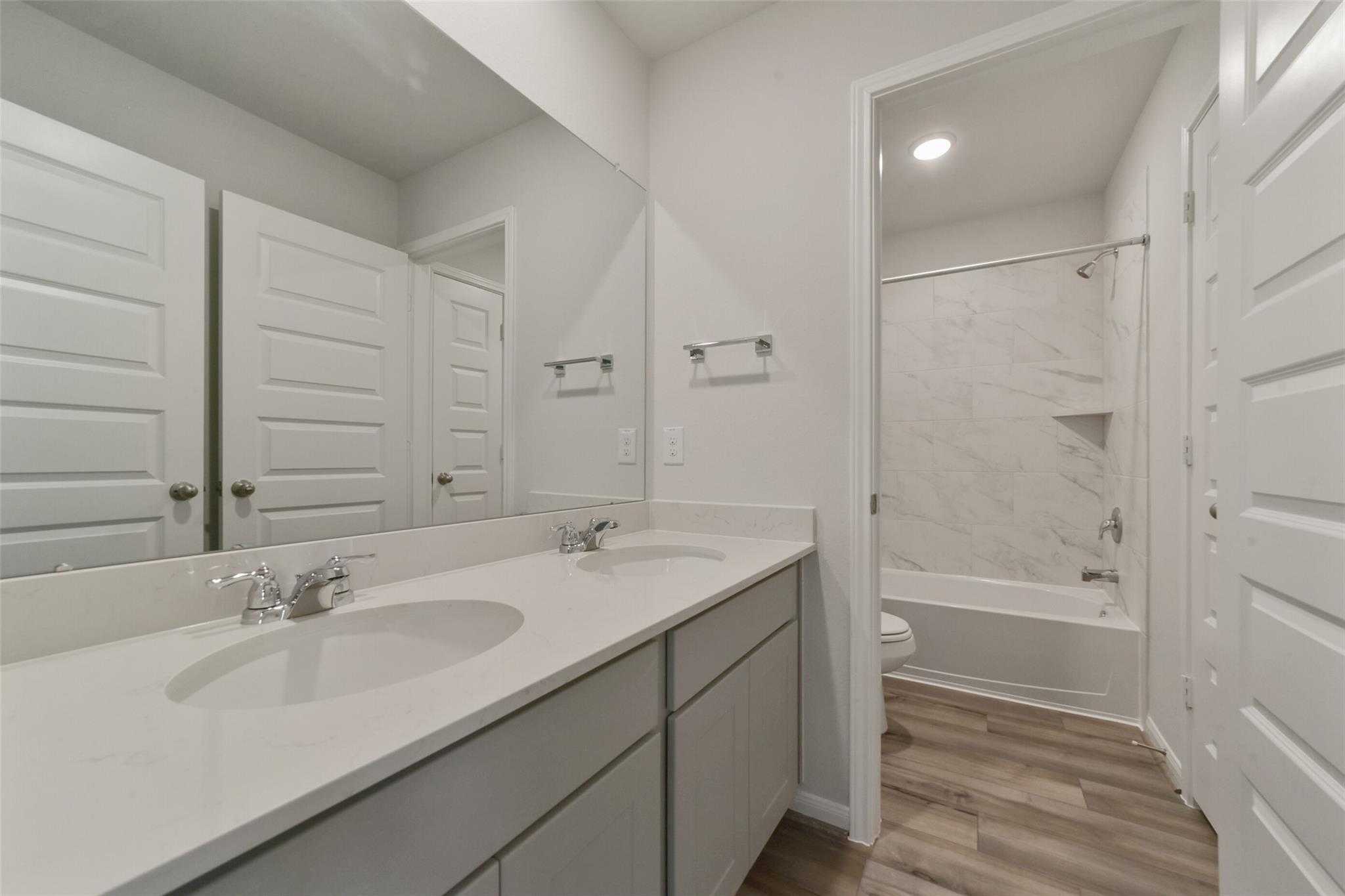 Modern bathroom with double vanity, bathtub, and tiled shower in 5-bedroom Davidson Homes San Marcos E, Beasley, Texas