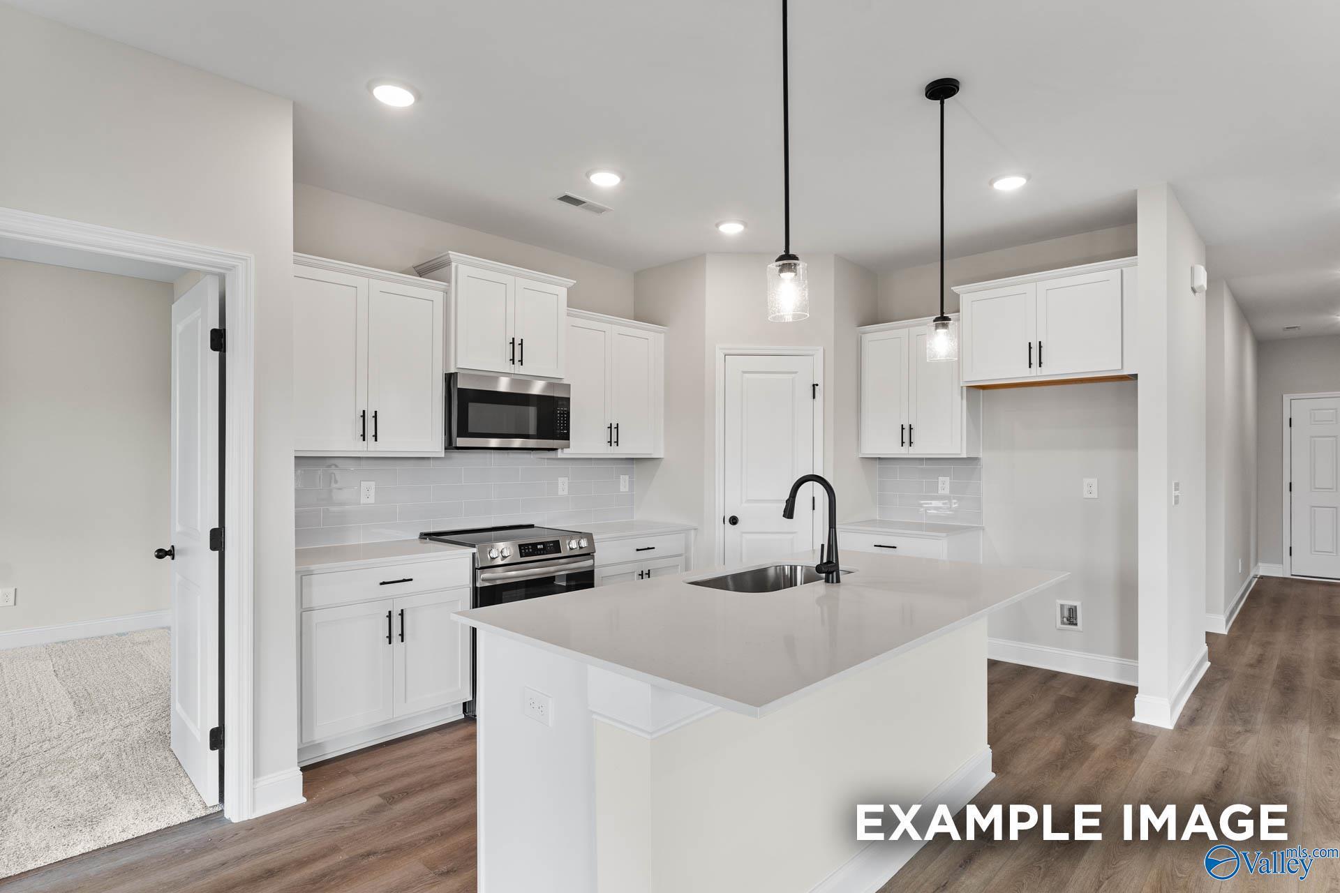Modern kitchen with white cabinets, quartz island, and stainless appliances in The Franklin B floor plan, Harvest, Alabama.