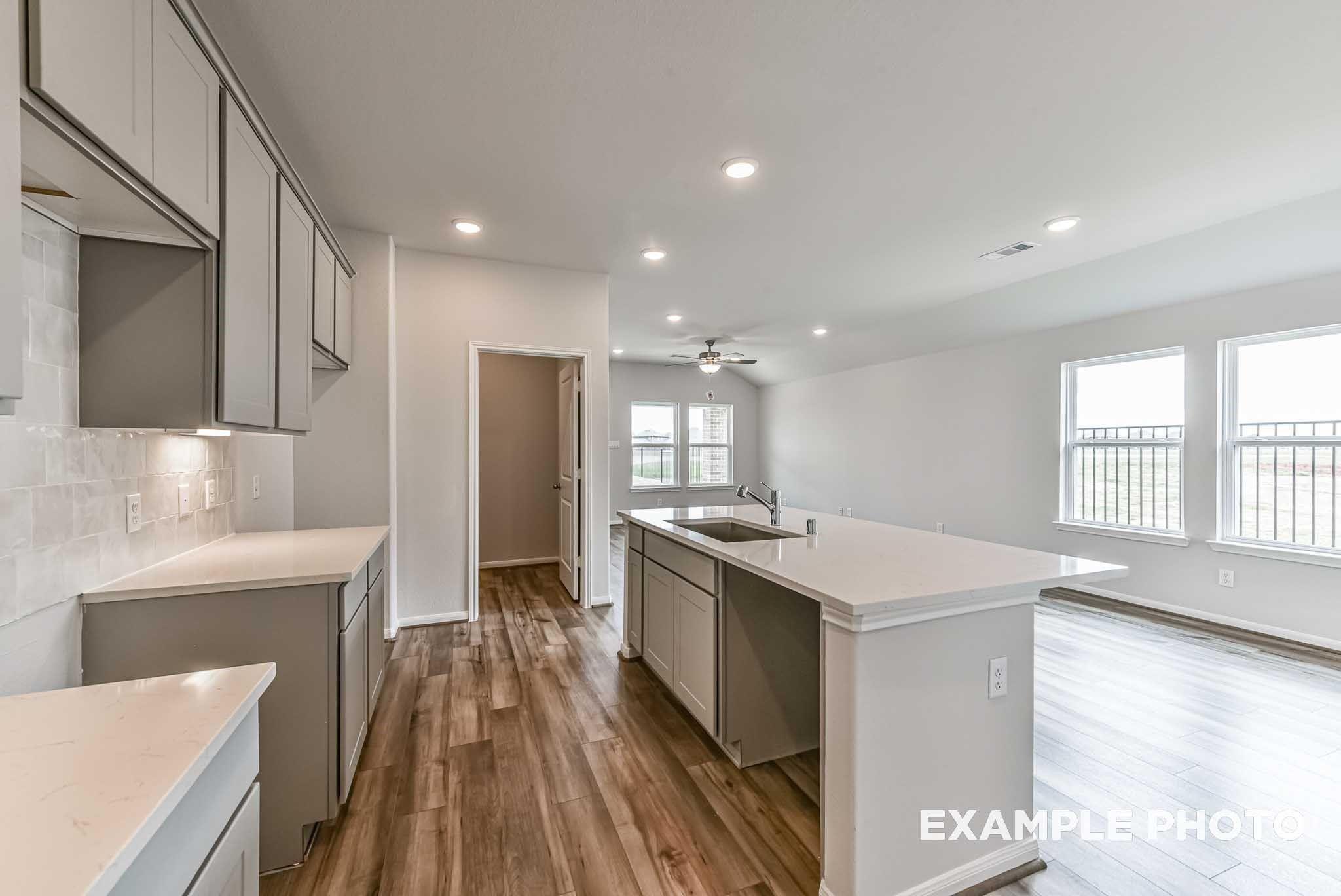 Open-concept kitchen with white cabinetry, island with sink, and wood-look flooring in The Costa A floor plan at River Ranch Meadows