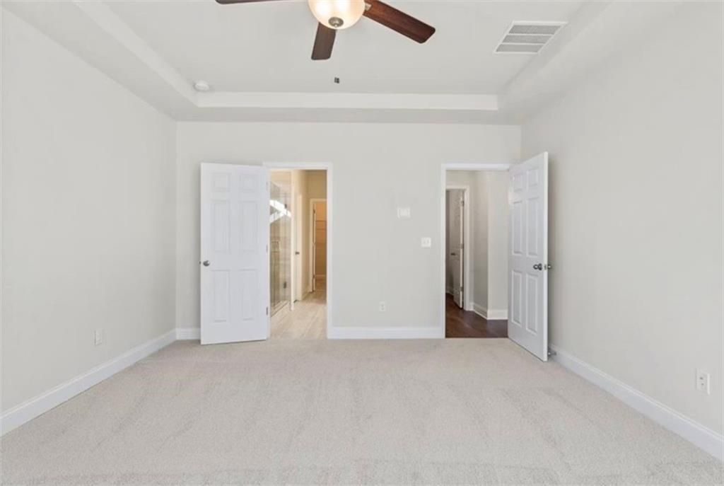 Spacious bedroom with tray ceiling and dual door access in The Ash C floor plan at Wehunt Meadows in Hoschton, Georgia.