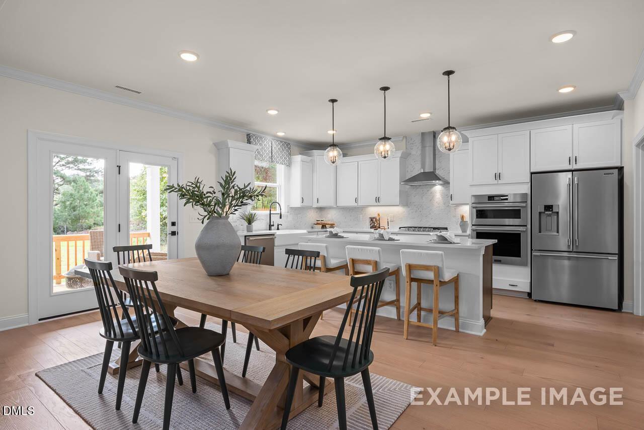 Open-concept kitchen and dining area with white cabinetry, stainless appliances, and farmhouse table in Davidson Homes Ashland, Apex NC