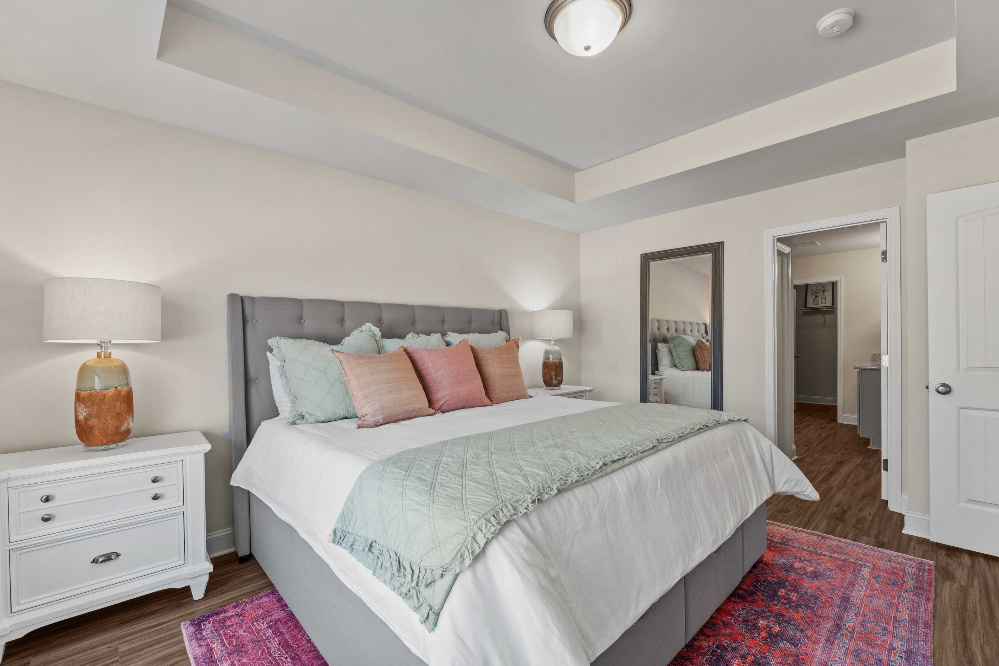 Spacious primary bedroom at Ramsay Cove in Owens Cross Roads AL with gray upholstered king bed, teal quilt, pink rug, and en-suite bath